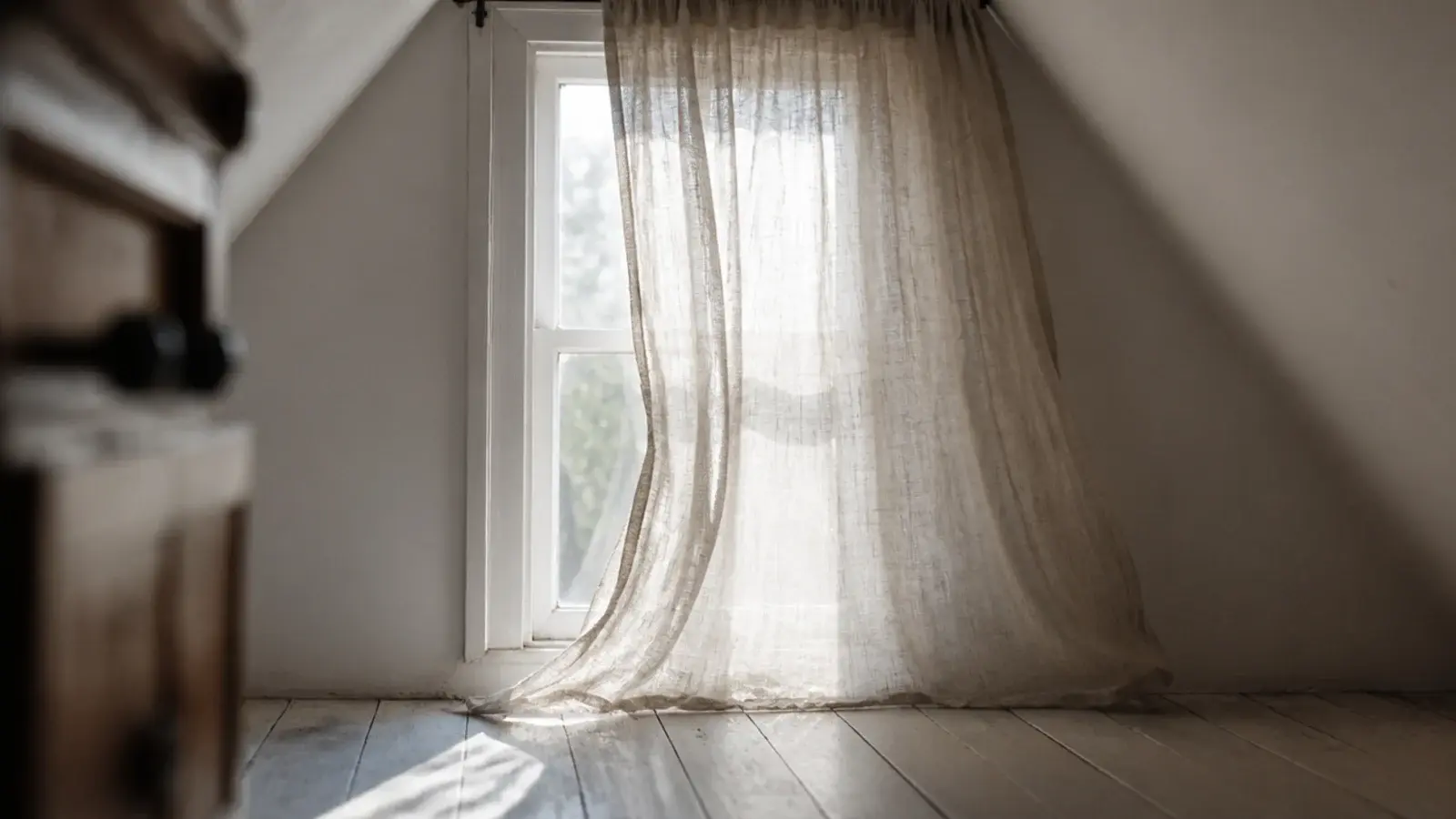 unlined linen curtain filtering daylight on an attic gable window