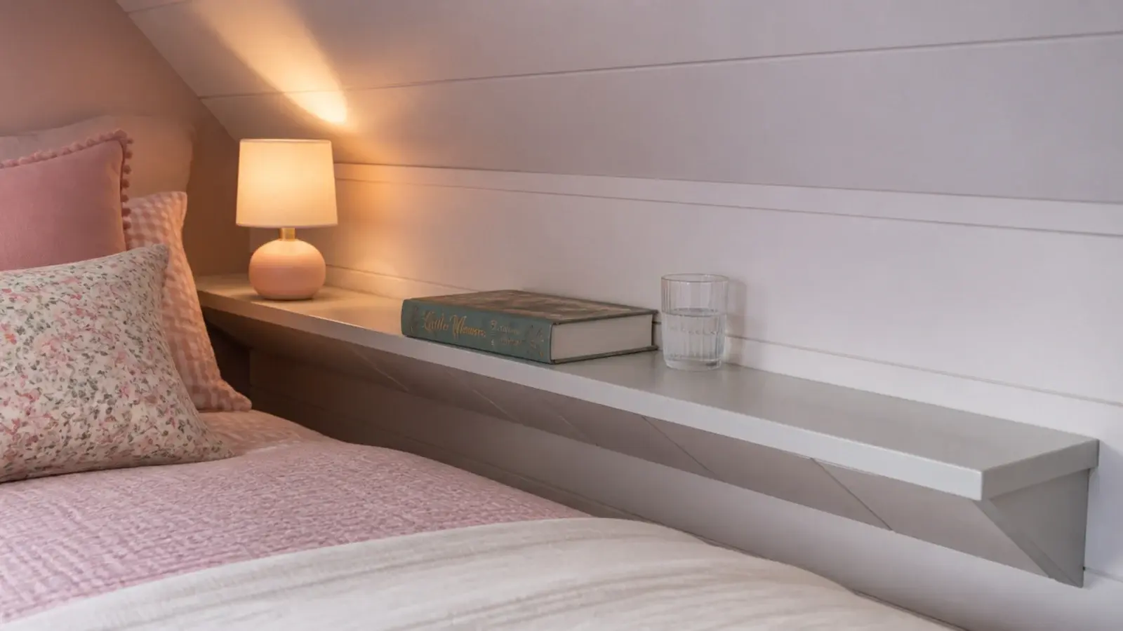 narrow shelf fixed to a knee wall beside a girls attic bed
