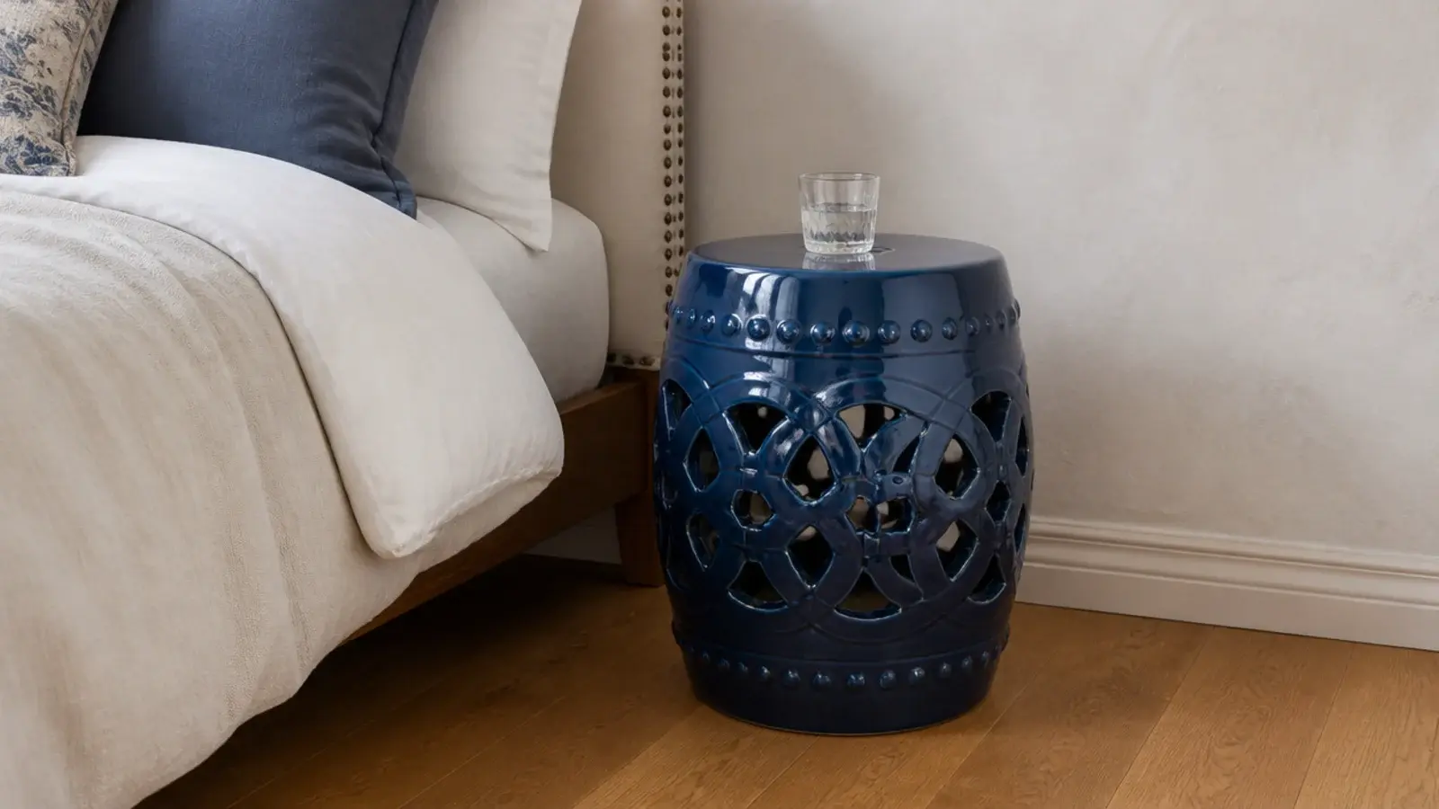 glazed ceramic garden stool in deep blue beside a linen bed