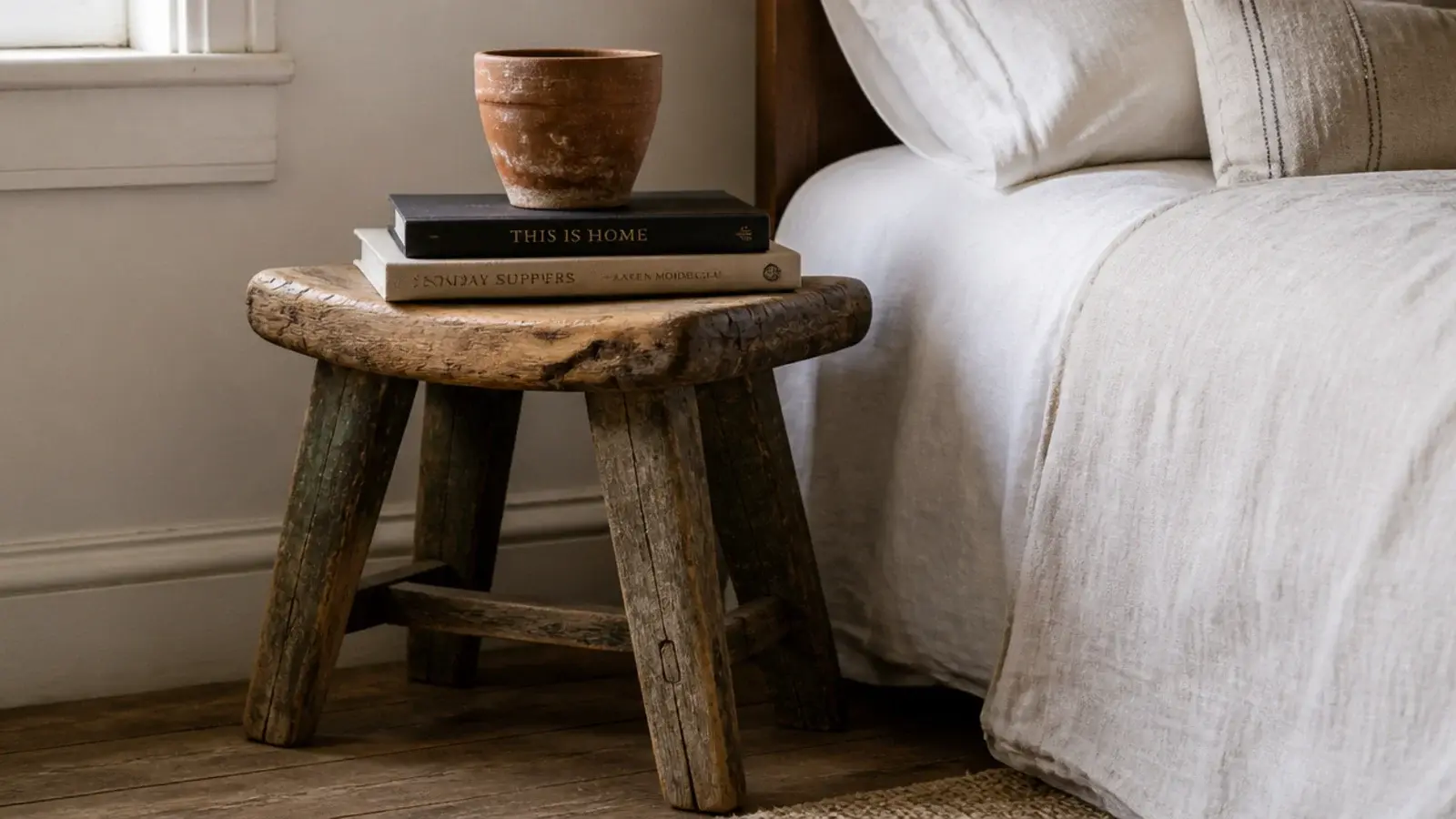 weathered wooden stool serving as a bedside table beside linen bedding