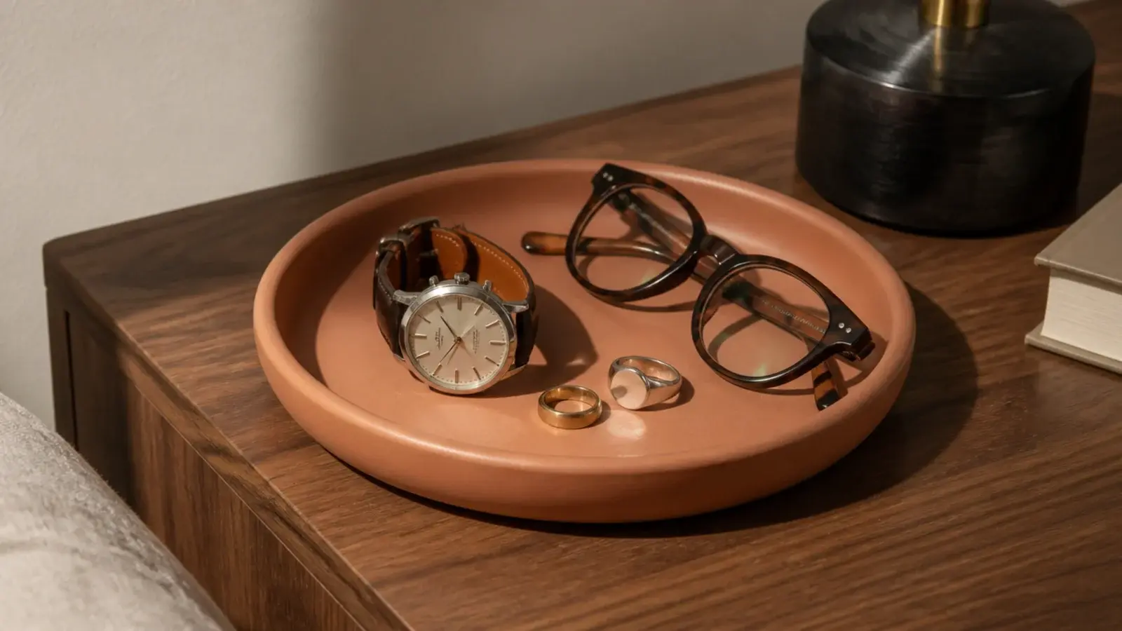 small clay tray on a bedside table holding rings and a watch