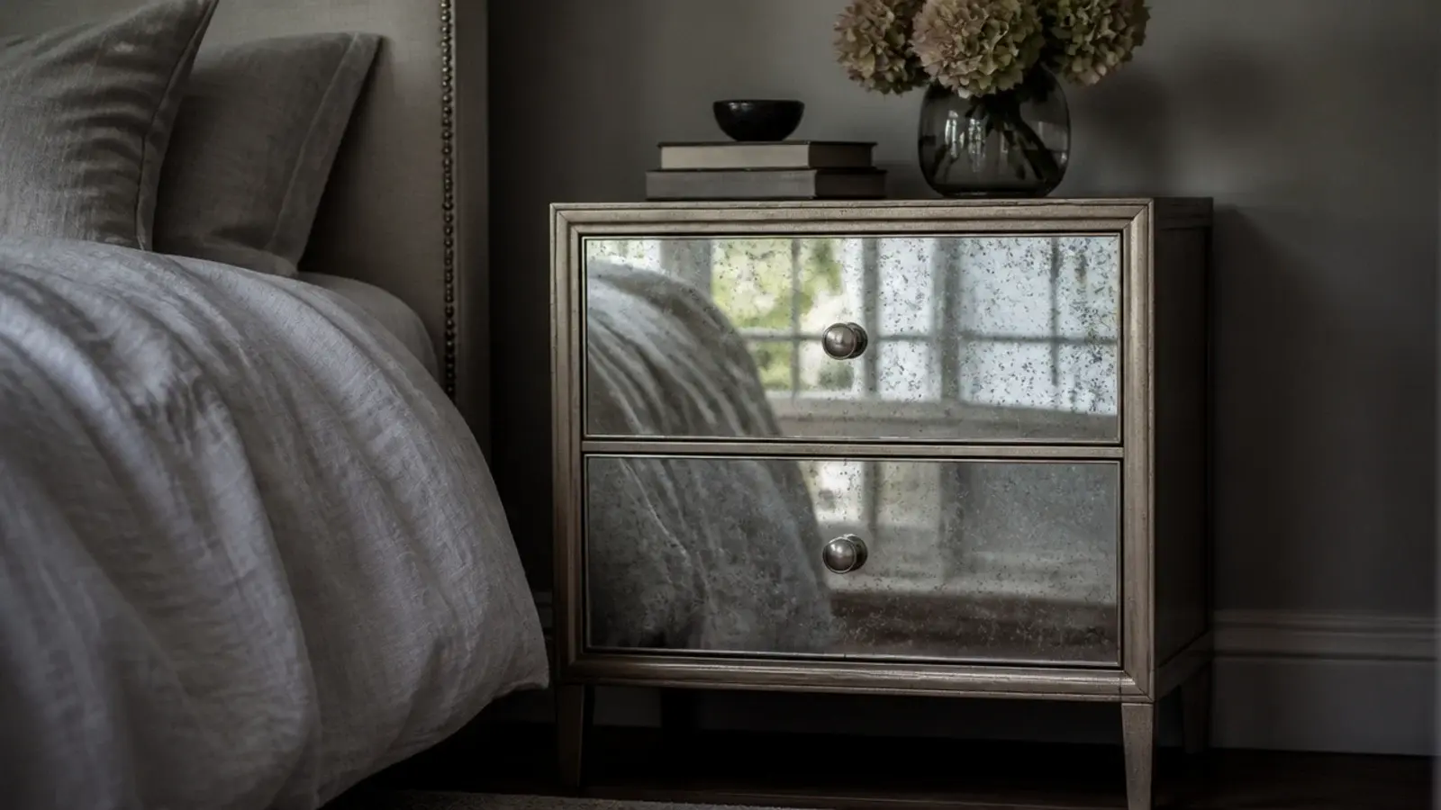 mirrored bedside drawers reflecting daylight in a dim bedroom corner