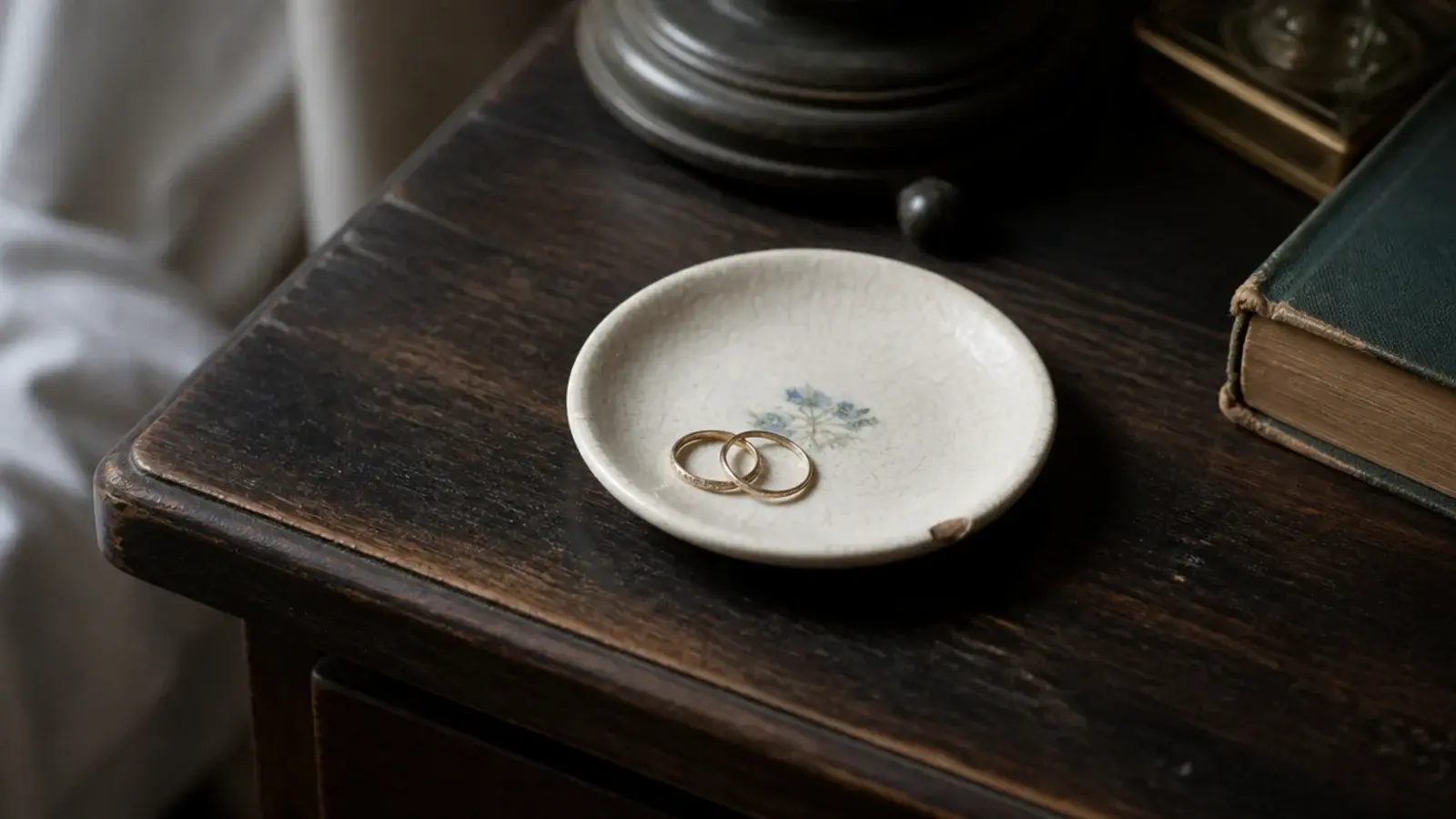 small chipped vintage saucer holding rings on a bedside table