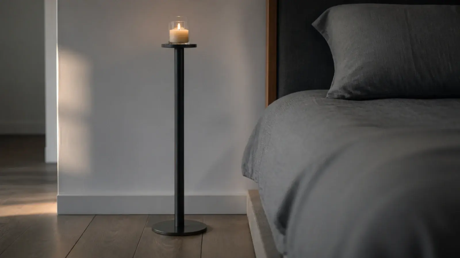 slim black column pedestal holding a small round top beside a bed