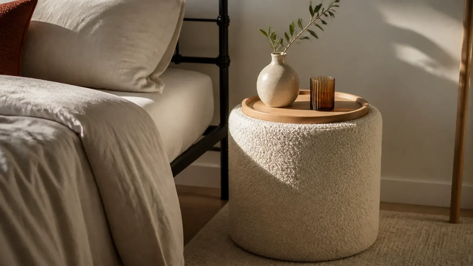 cream boucle covered drum table adding texture beside a hard bed frame