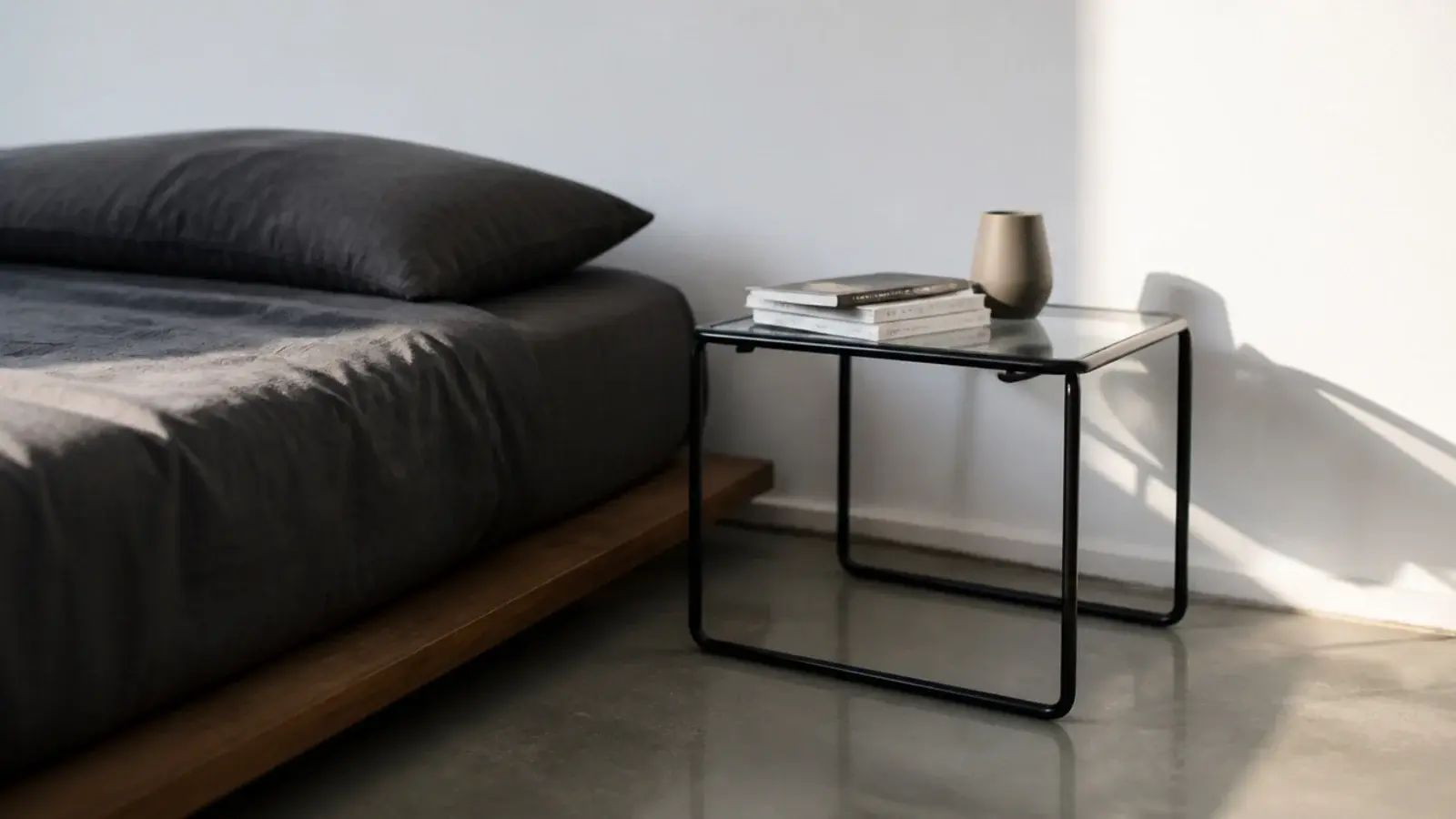 modern bedside table in tube steel and glass beside a low platform bed