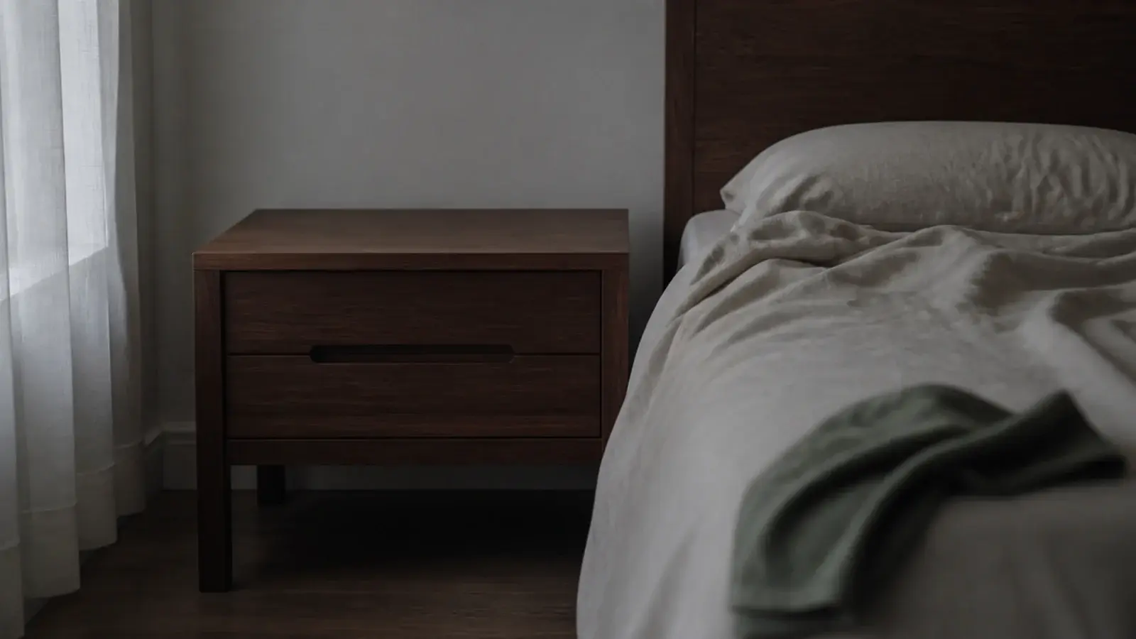 completely empty wooden bedside table beside an unmade bed