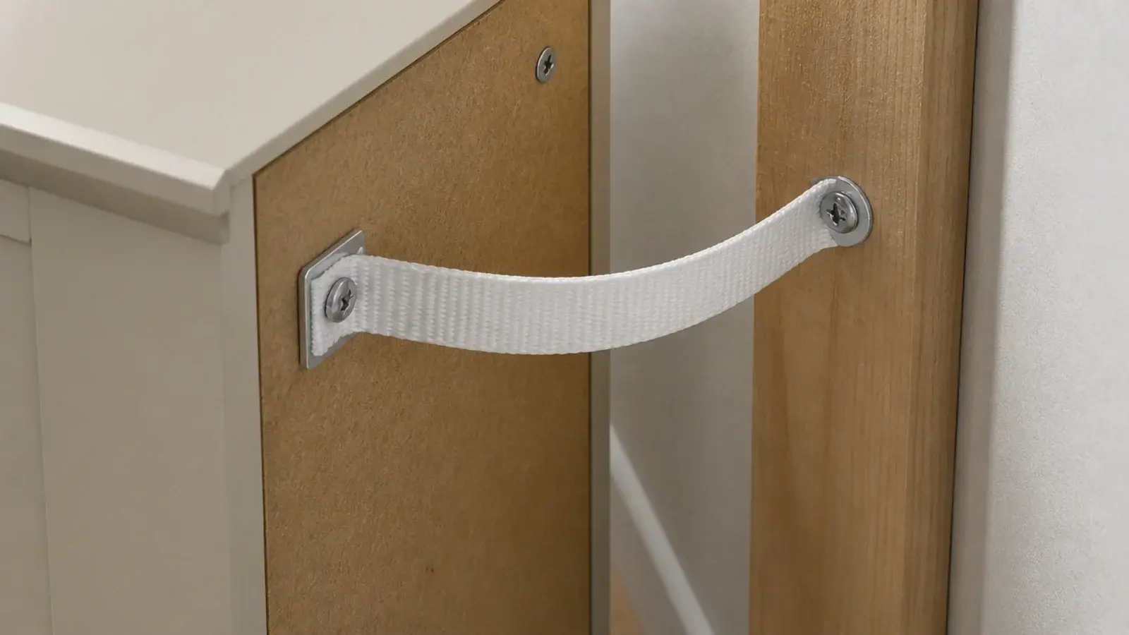anti tip strap fixed between a tall narrow cabinet and the wall