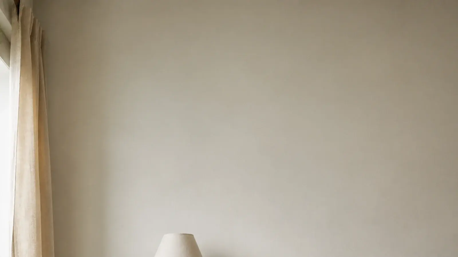 vertical image of a calm bedroom bookshelf beside a linen dressed bed