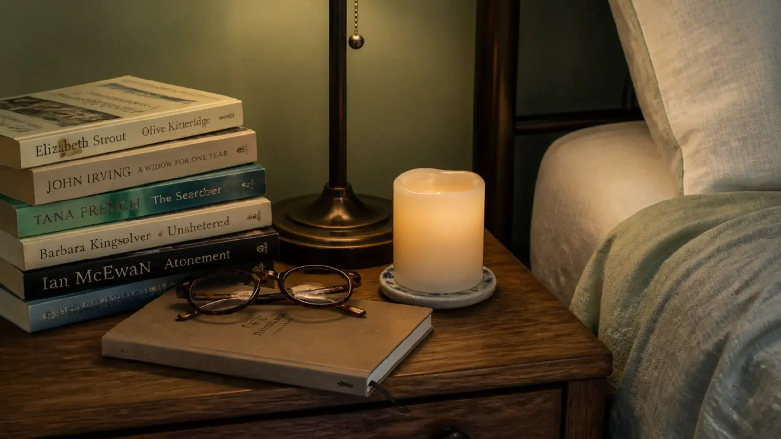 stack of books beside a flameless candle on a crowded nightstand
