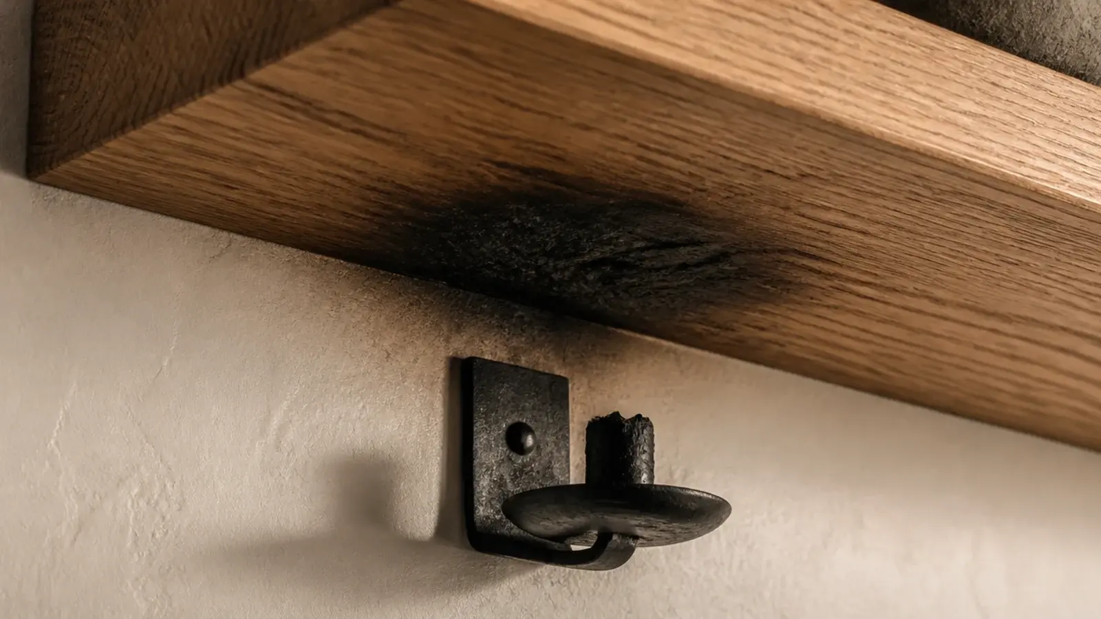scorched underside of an oak floating shelf above a wall candle holder