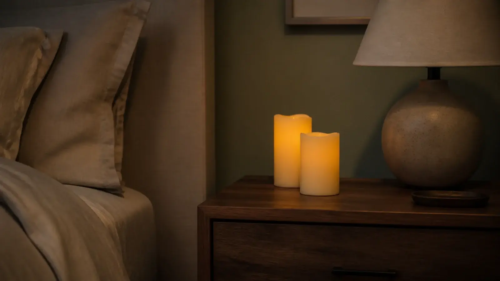 flameless wax pillars glowing on a bedside table beside a linen bed
