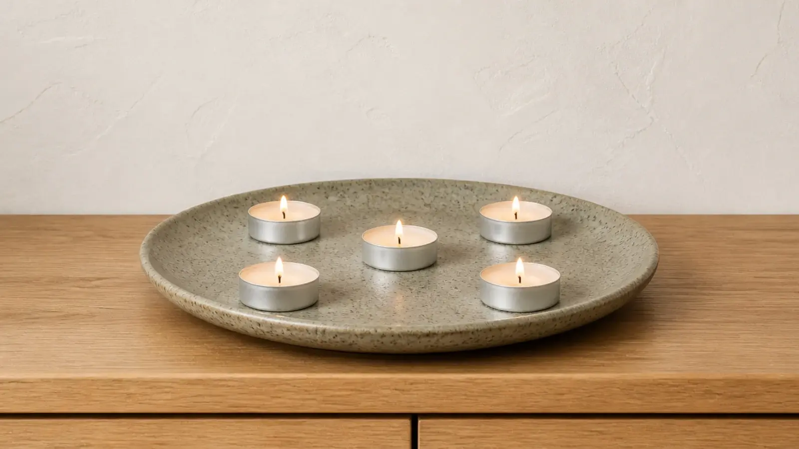 row of tealights in metal cups spaced across a speckled stoneware plate