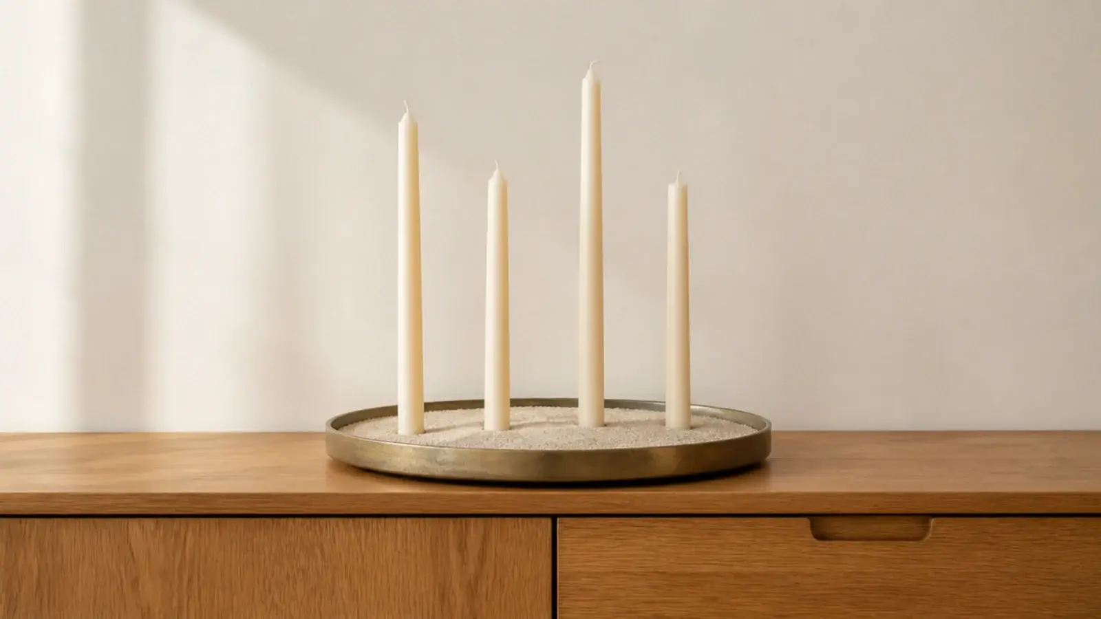 shallow tray filled with pale sand holding slim tapers upright in a cluster