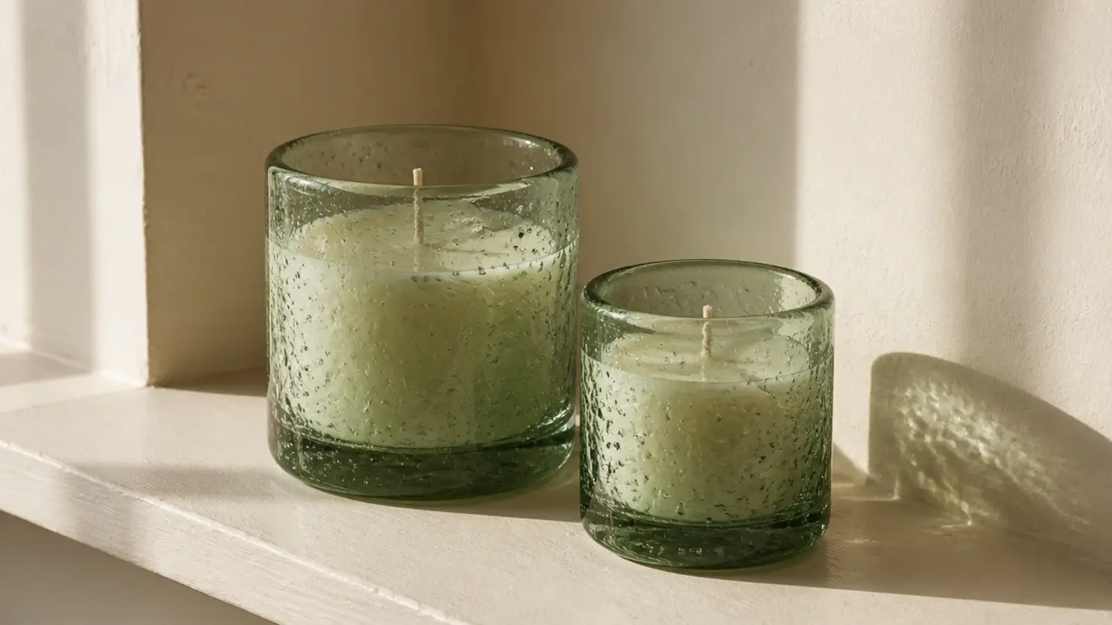 pale recycled glass candle vessels catching light on a windowsill ledge