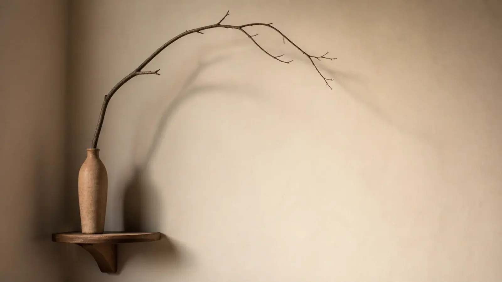 bare curved branch arranged in a tall clay vessel on a corner shelf