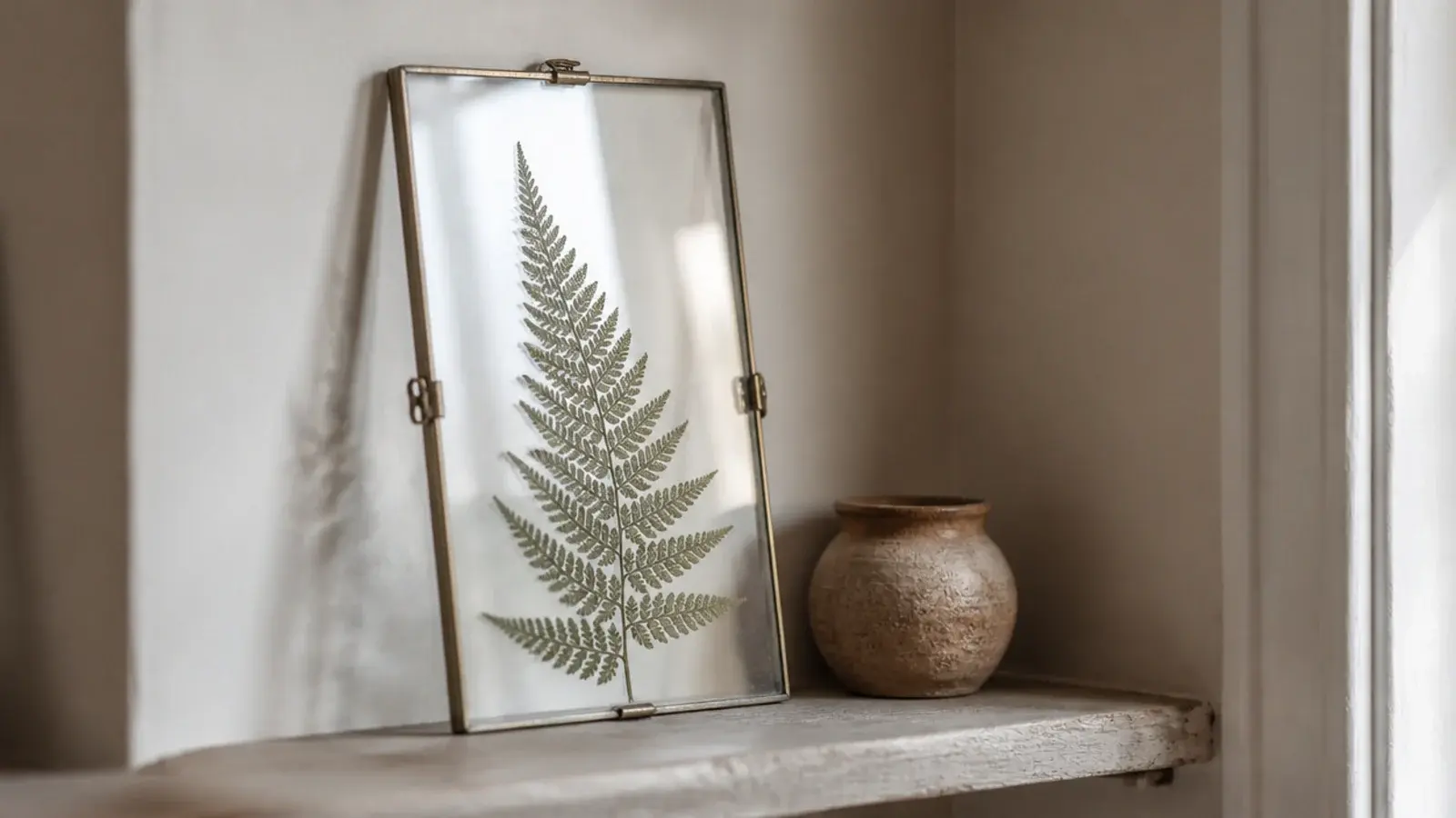 pressed fern leaf in a simple glass clip frame leaning on a shelf