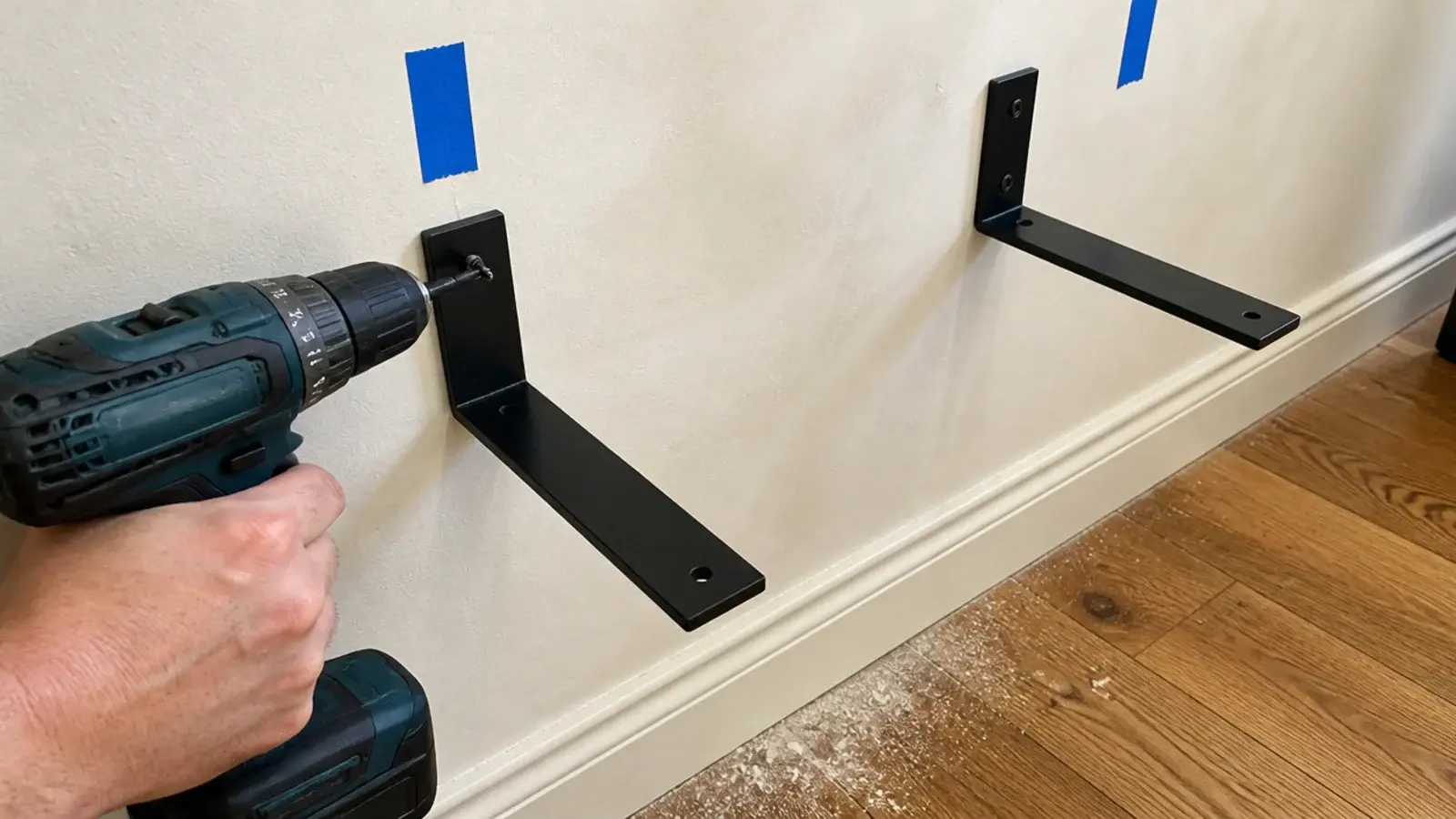 black metal bracket being screwed into a wall corner for shelves