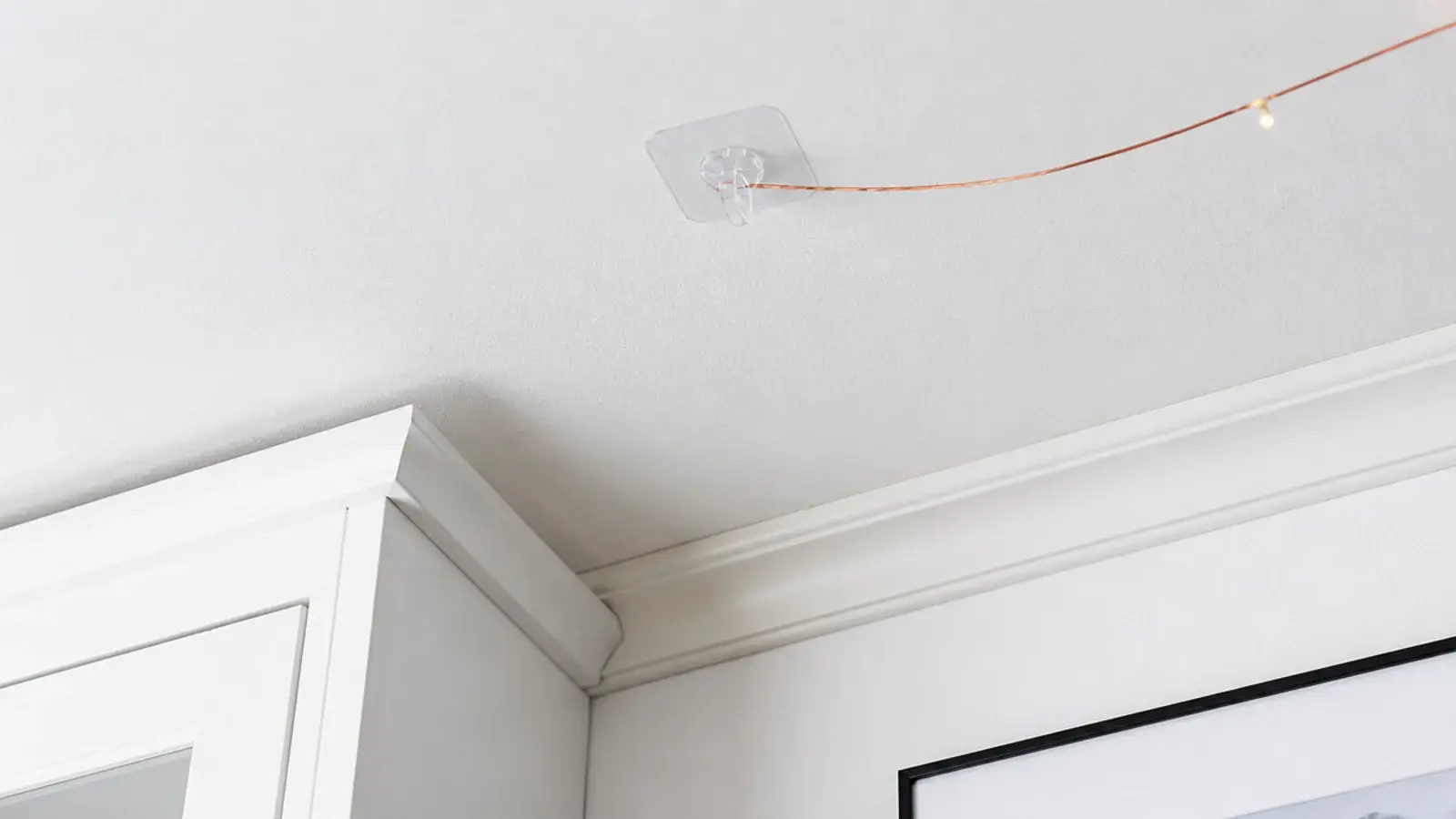 clear adhesive hook on a ceiling holding a fine light wire