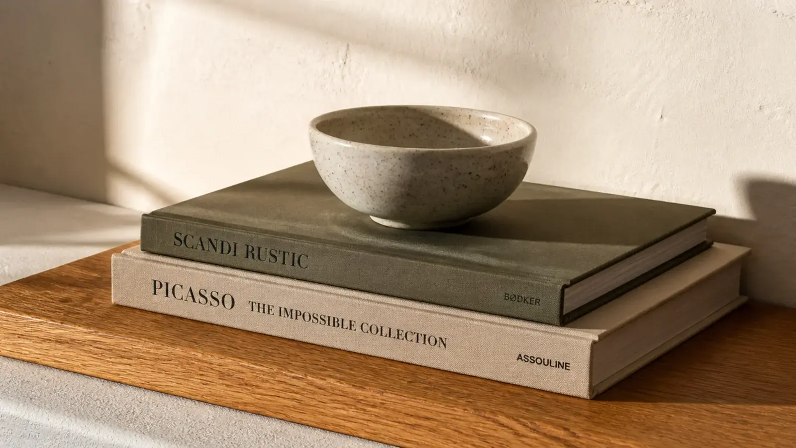 two hardback books lying flat under a small ceramic bowl on a shelf