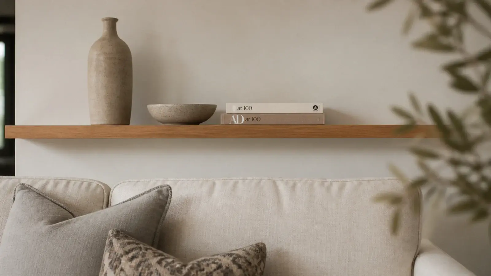 one long oak shelf above a linen sofa holding three grouped objects