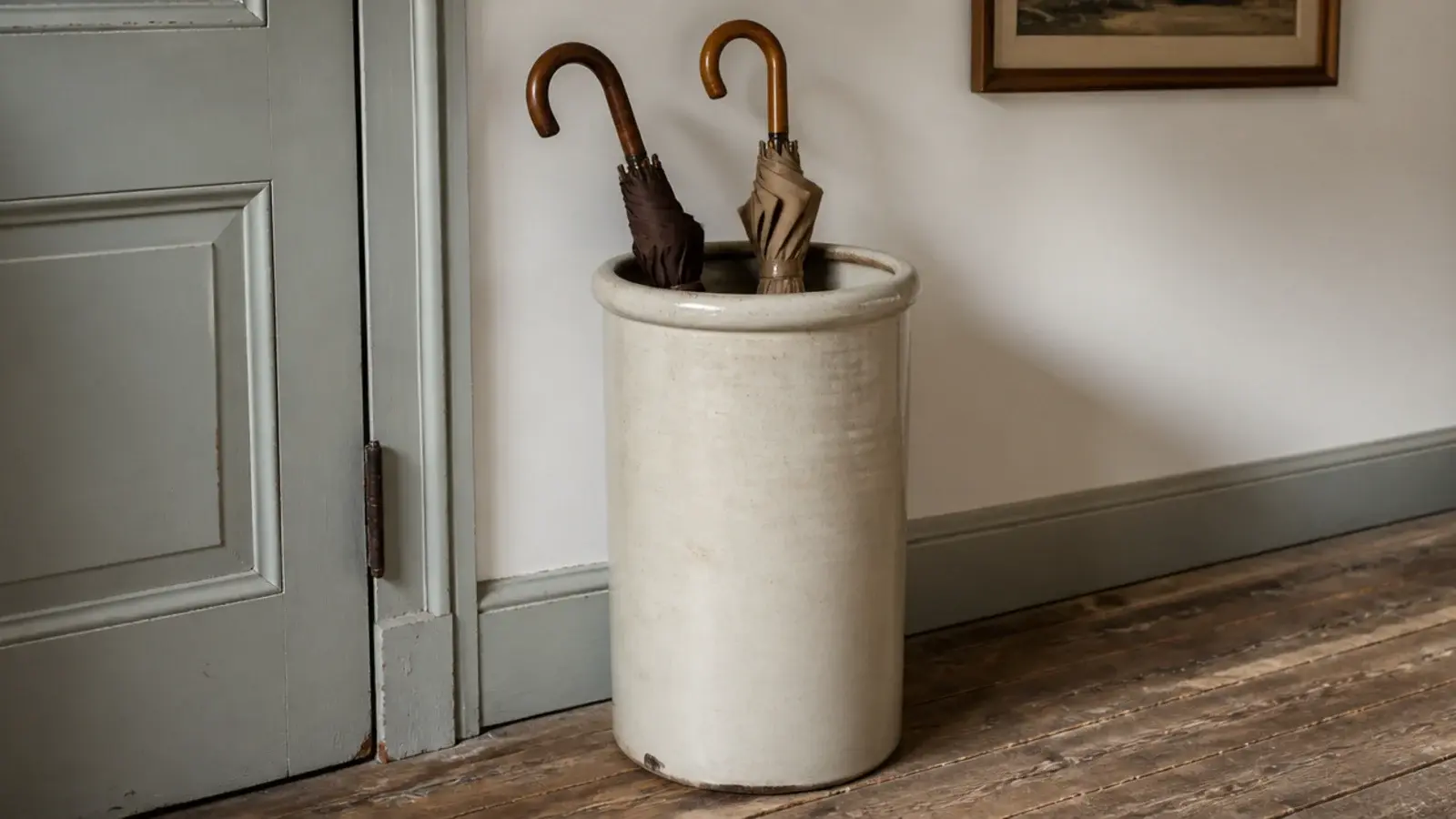 tall cream stoneware crock holding umbrellas in a farmhouse entry