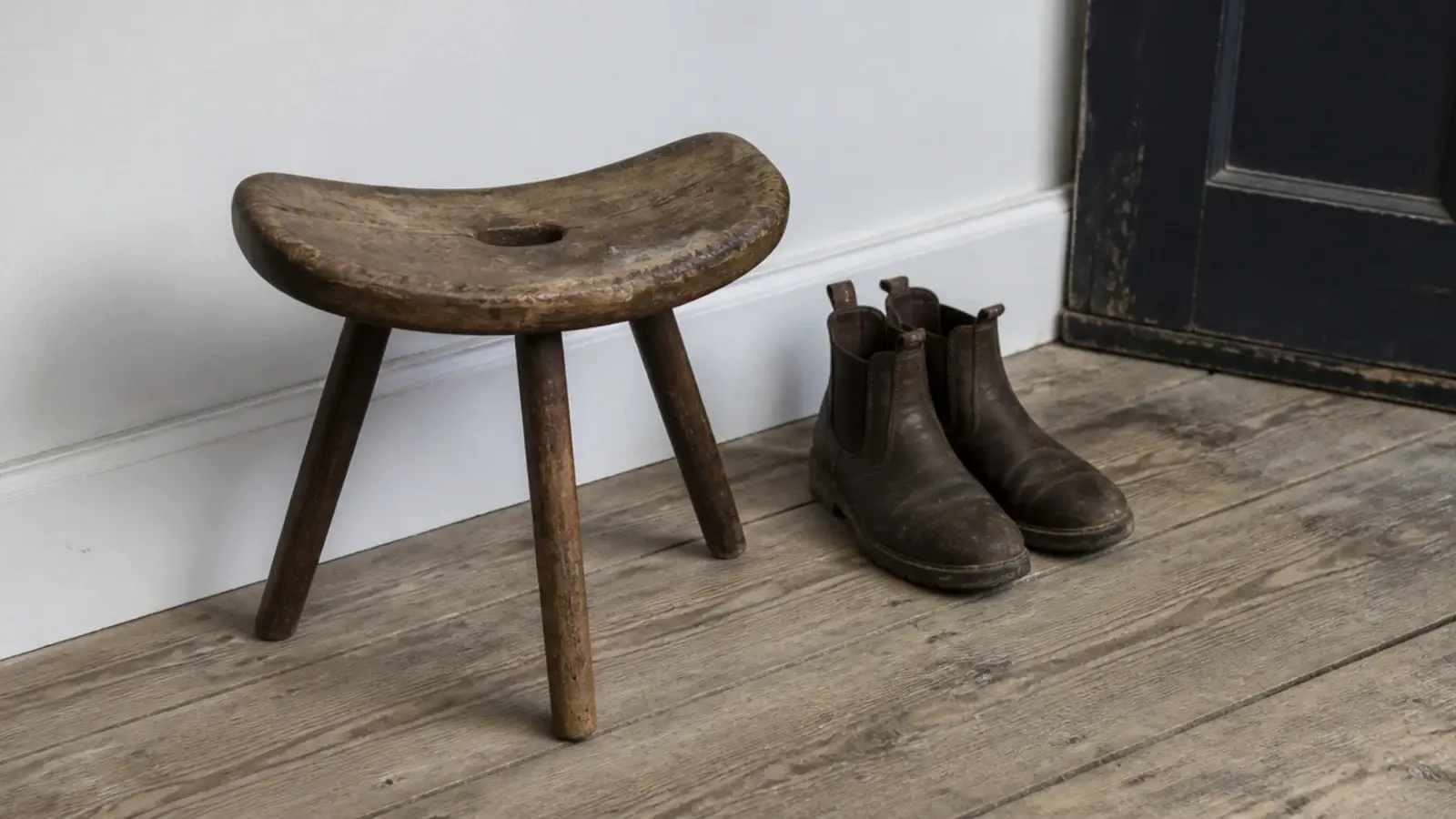 single antique wooden stool anchoring a simple farmhouse entryway