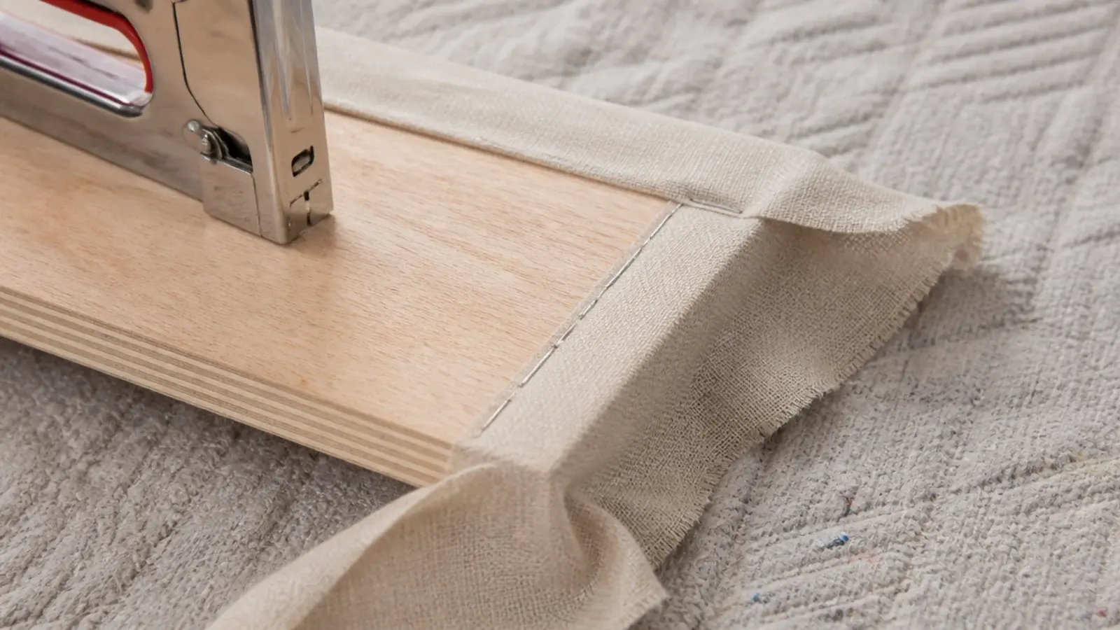staple gun tensioning linen fabric along the back of a headboard panel