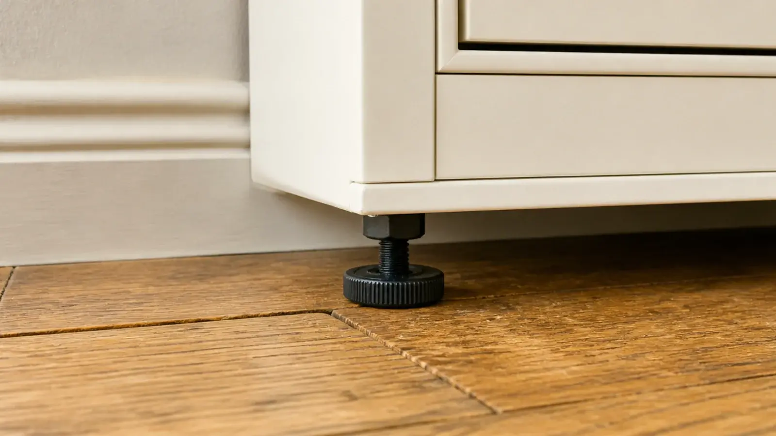 adjustable cabinet foot resting on uneven oak boards under a cabinet