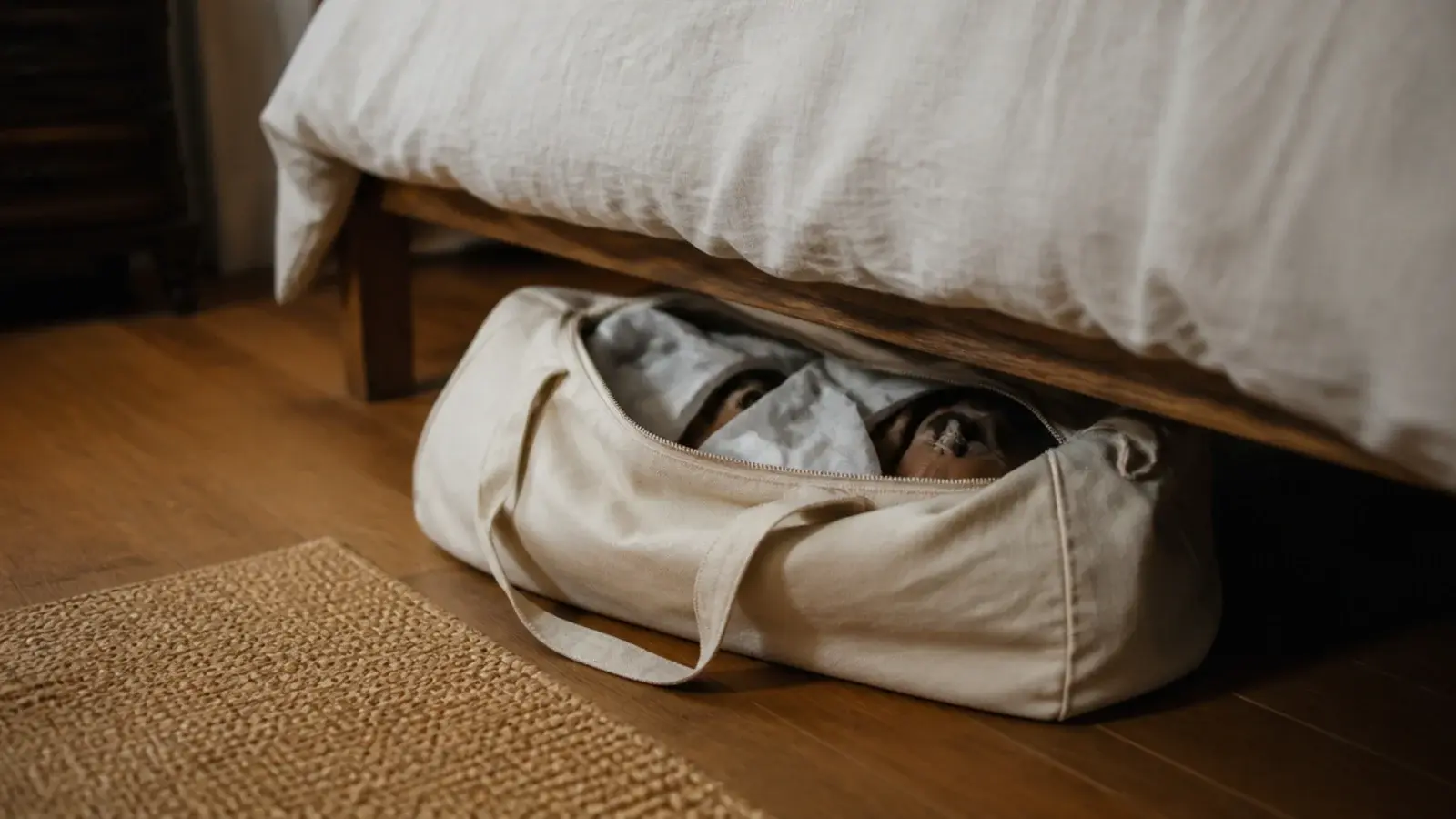 canvas duffel of out of season shoes stored under a linen bed