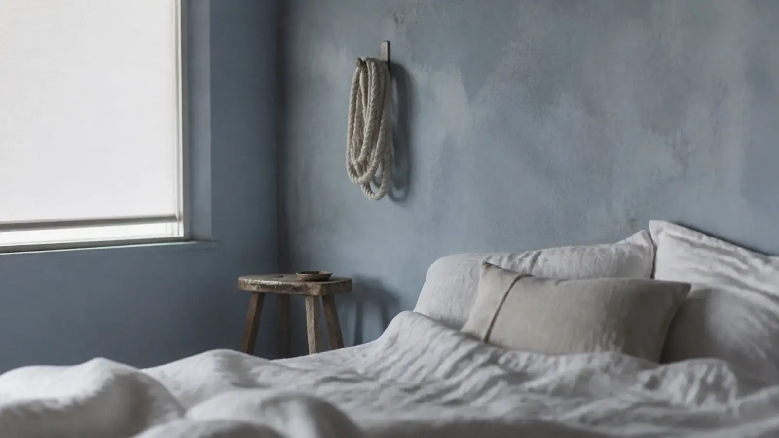 washed blue grey wall with linen bedding and pale rope details