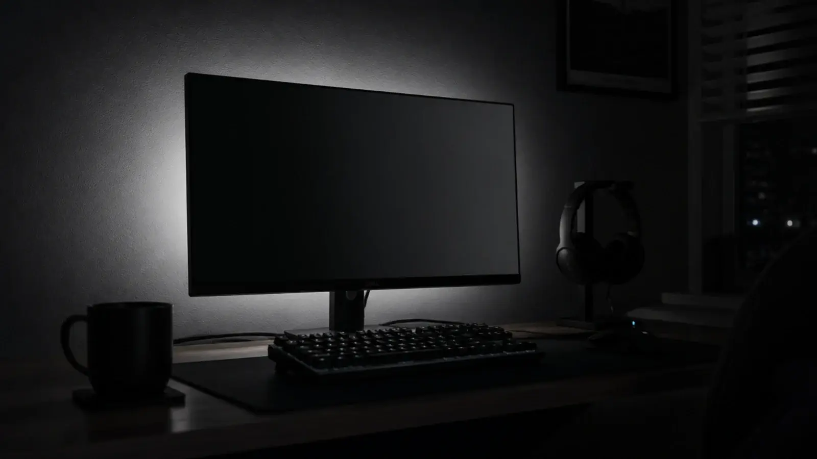 neutral white glow behind a monitor lighting a dark bedroom wall