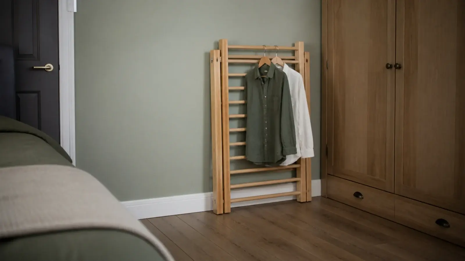 folding drying rack collapsed flat against a bedroom wall