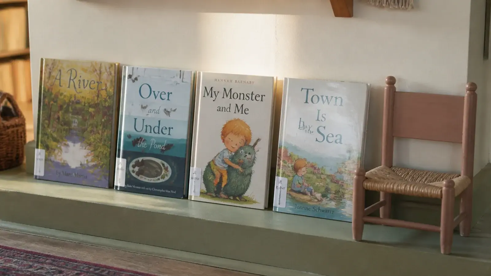 library books standing cover outward on a low shelf beside a chair