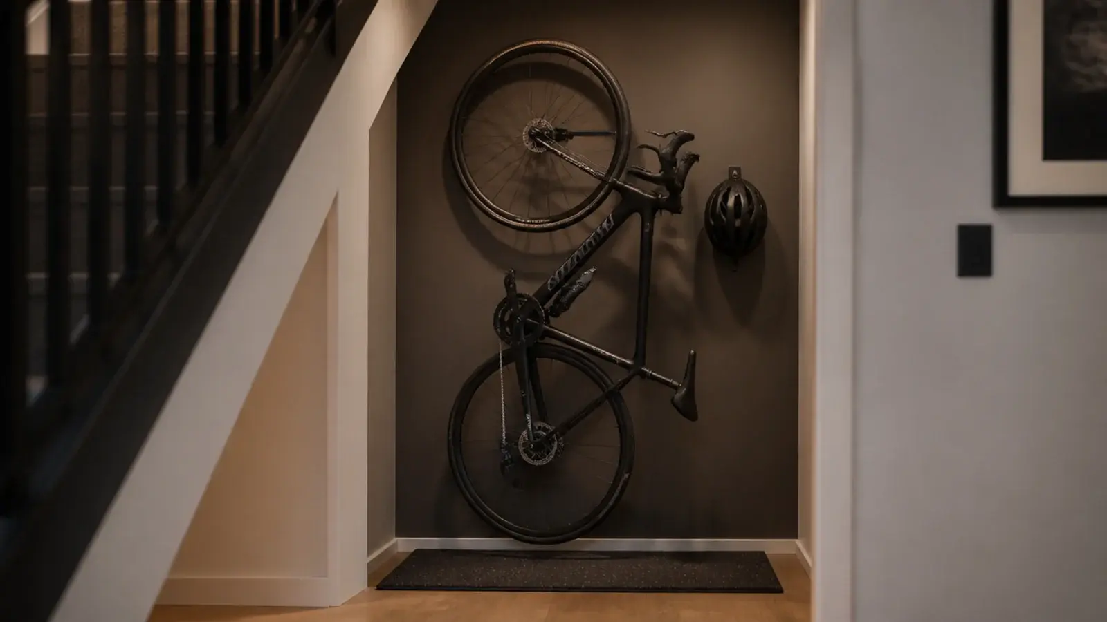 bicycle hanging vertically from a wall hook under a staircase
