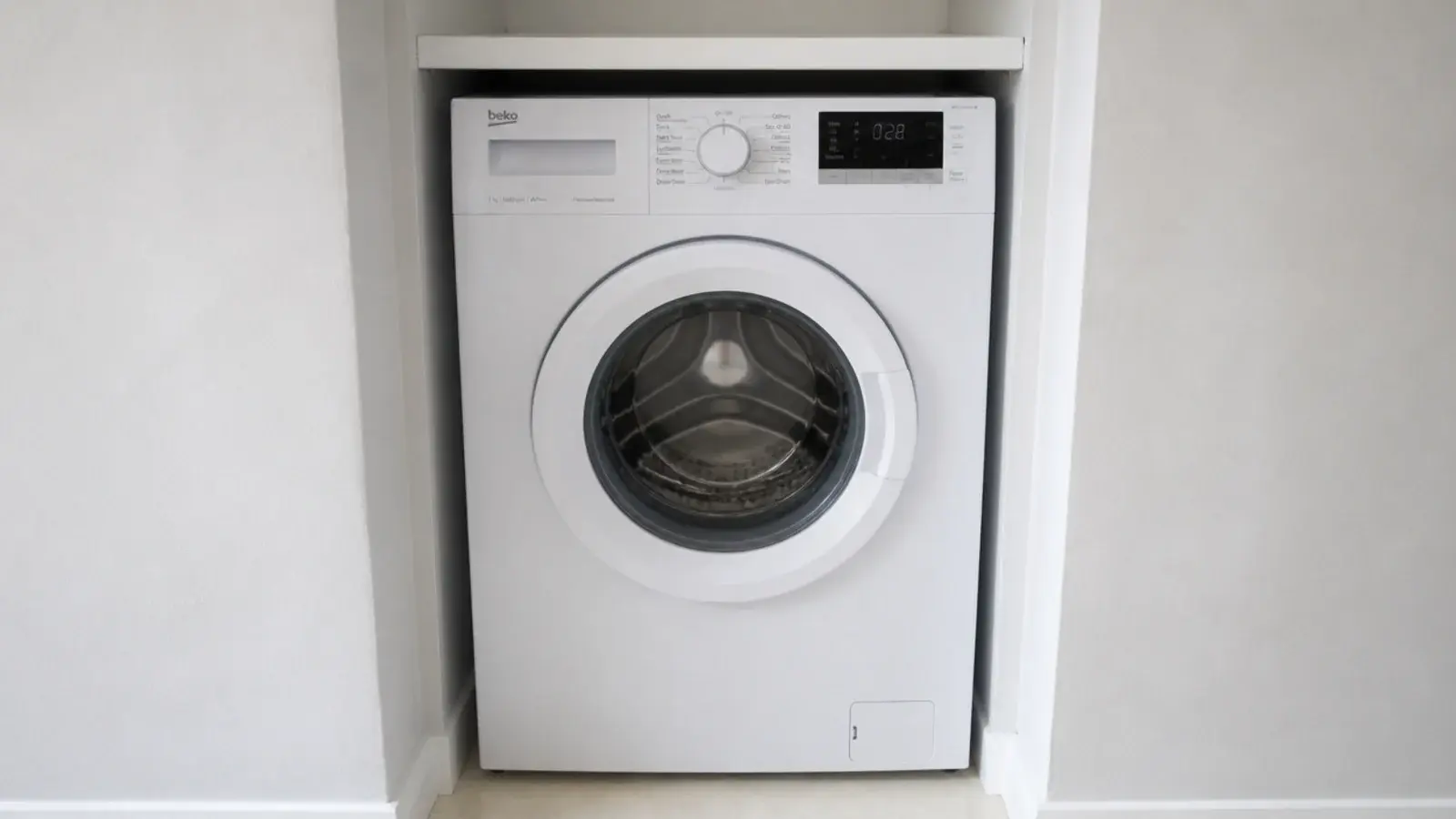 slim european washing machine slotted into a narrow alcove beside shelving