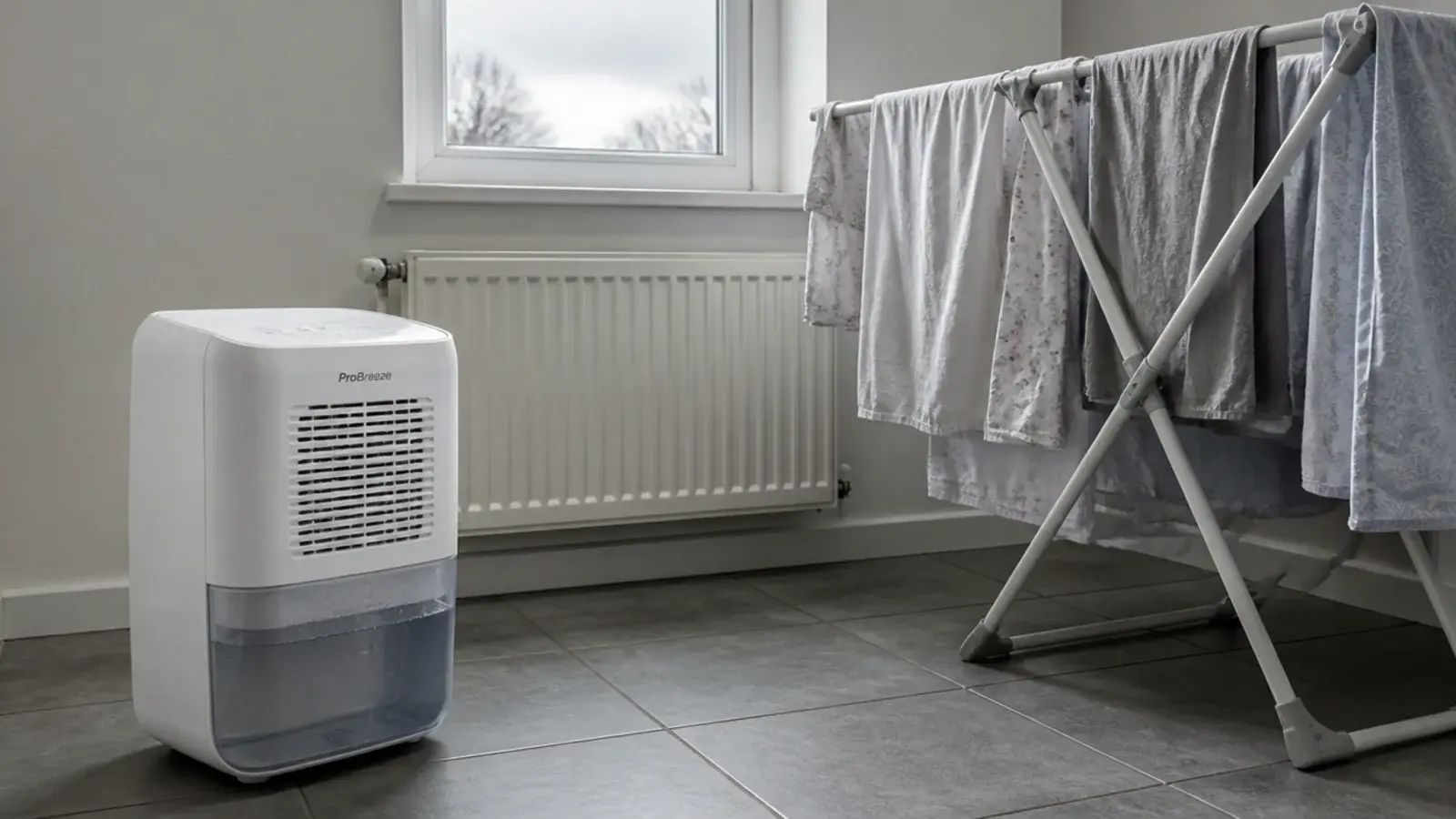 compact dehumidifier running beside a loaded airer of damp bed linen