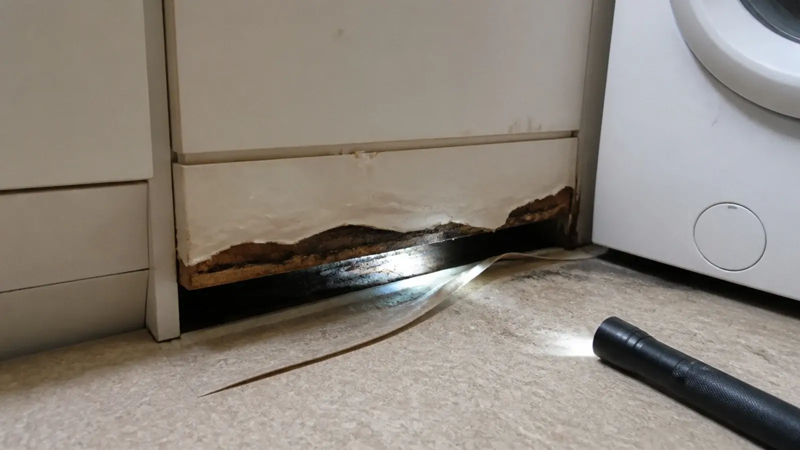 swollen cabinet plinth and lifted vinyl beside a leaking washer
