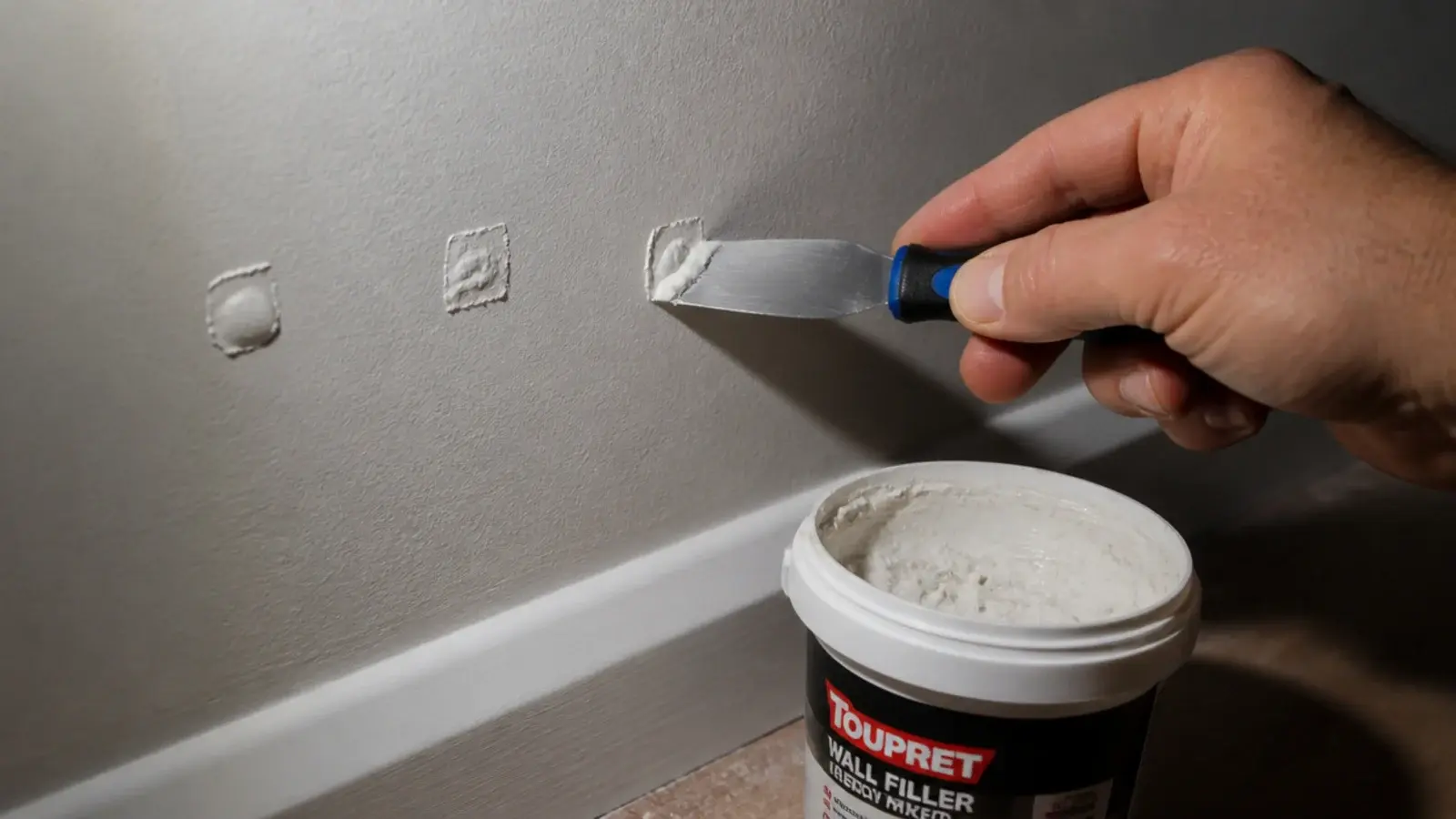 filler knife smoothing filler into a small screw hole in a painted wall