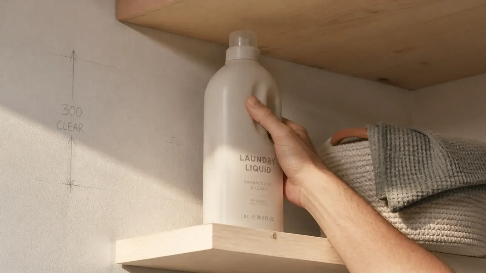 hand lifting a tall bottle clear between two widely spaced timber shelves