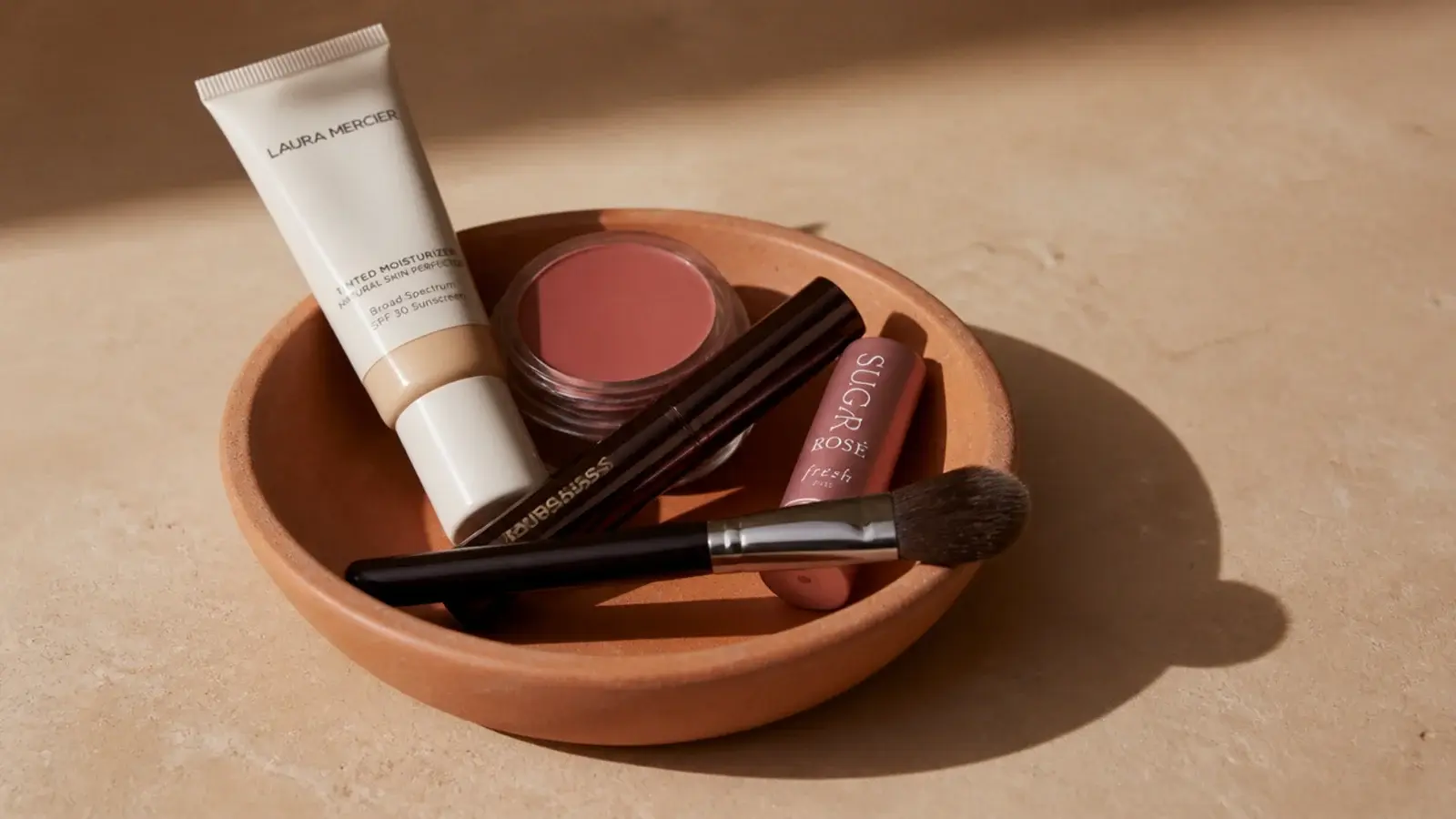 five everyday makeup products grouped in a small clay dish