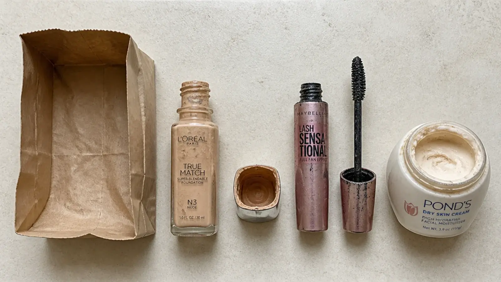 old mascara and separated foundation lined up beside a small paper bag