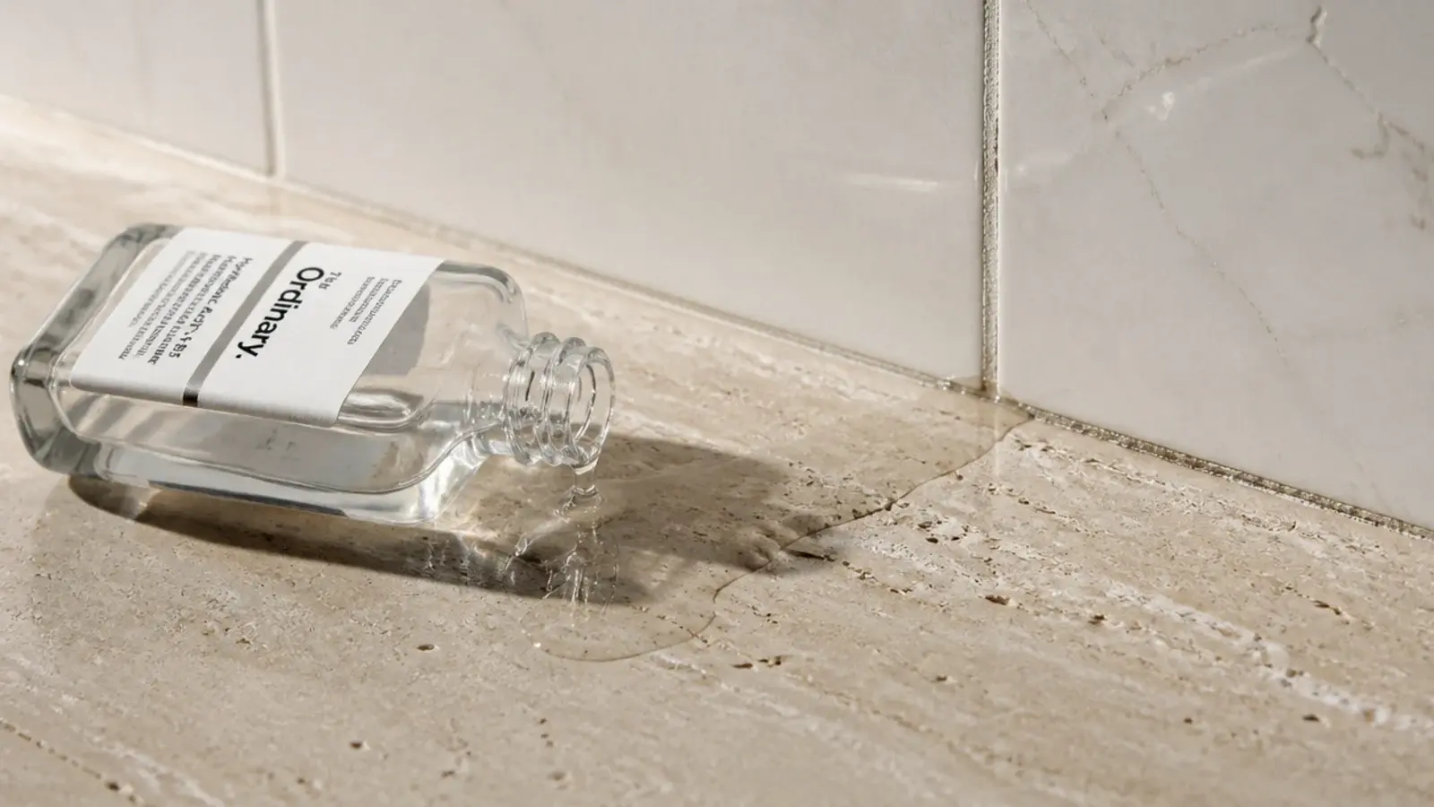 spilled serum running across a bare vanity counter with no tray edge