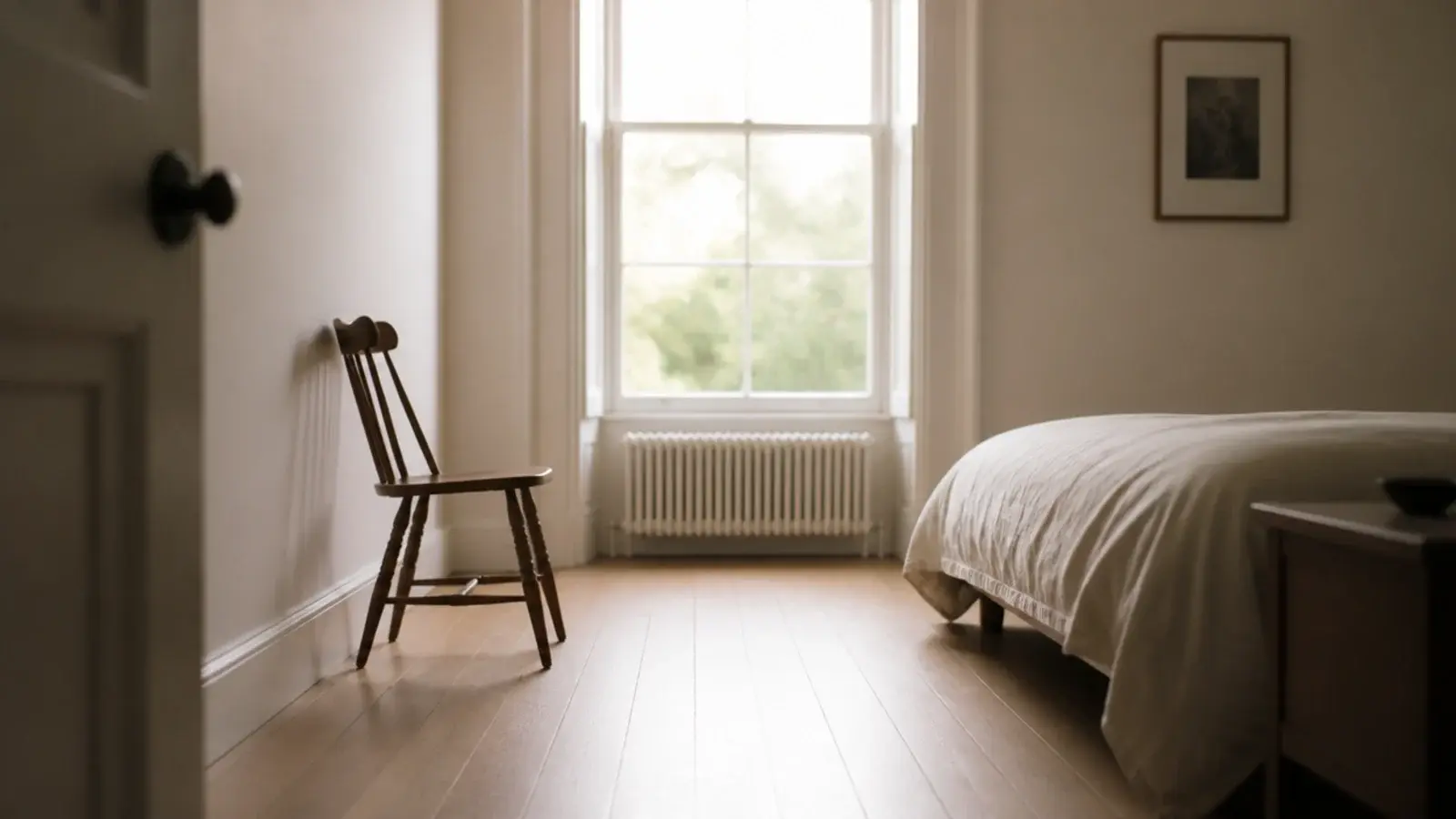 bedroom floorboards running away from a bright window toward the bed