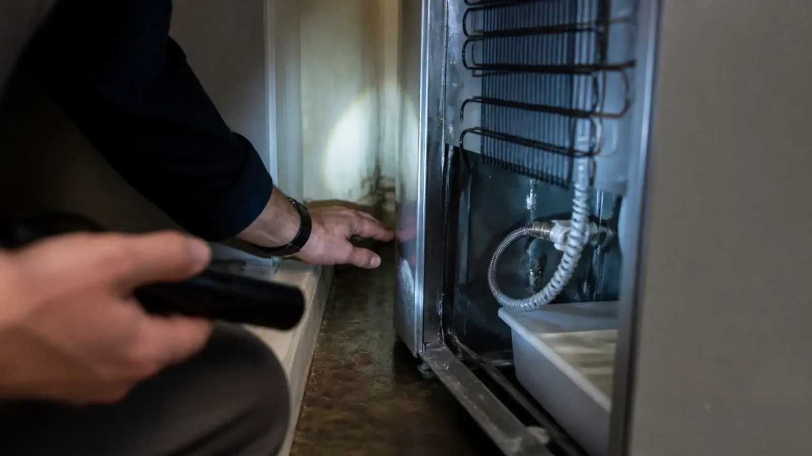hand checking behind a fridge for a damp patch on kitchen boards