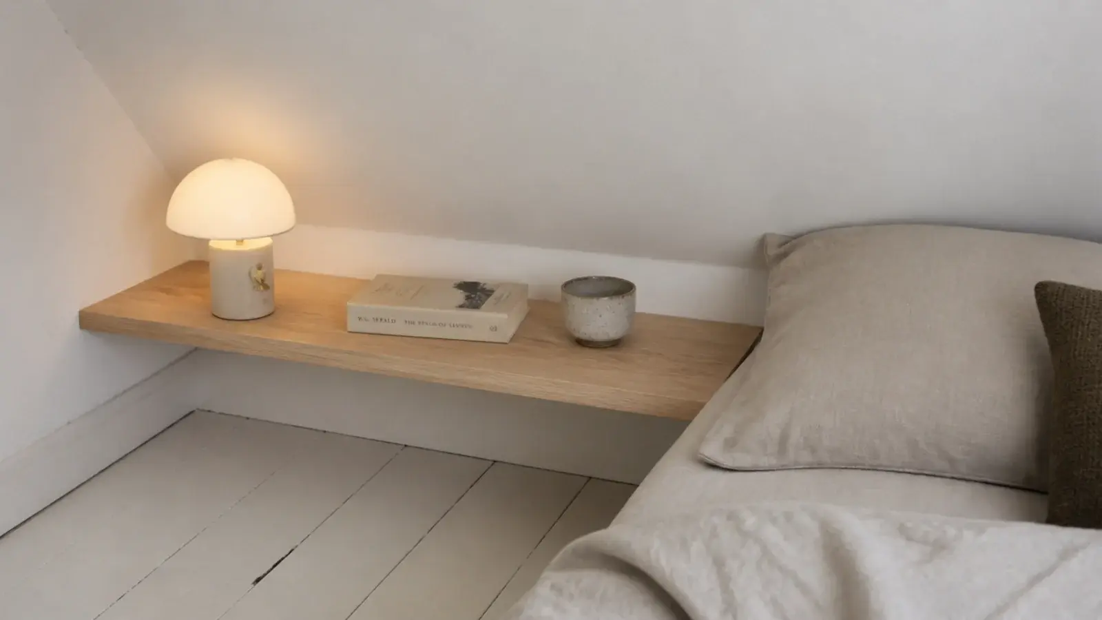 short floating shelf fixed beside a small attic bed holding a lamp