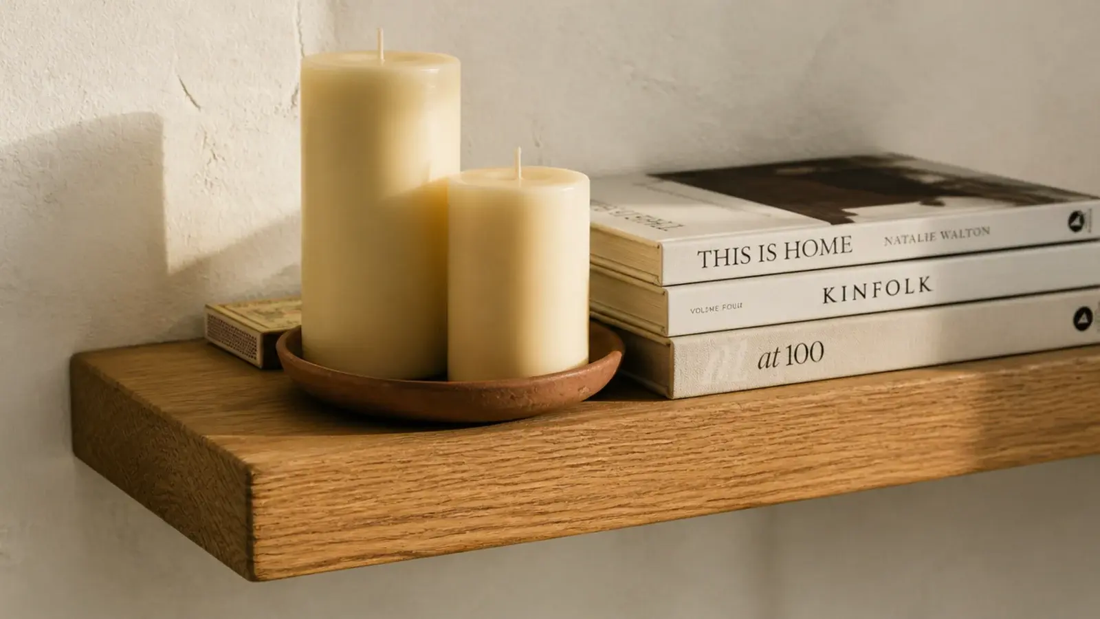 two pillar candles and a clay dish styled on an eye level bookshelf