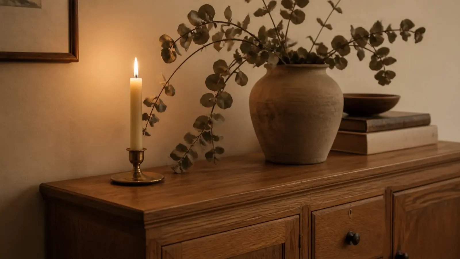dried eucalyptus stems leaning close to a burning taper on a sideboard