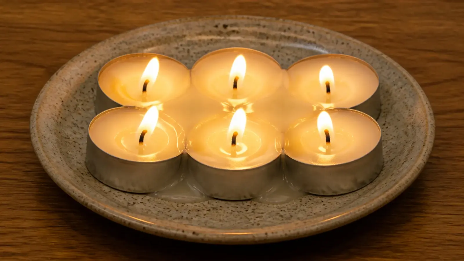 tealights pushed shoulder to shoulder on a plate with pooling wax