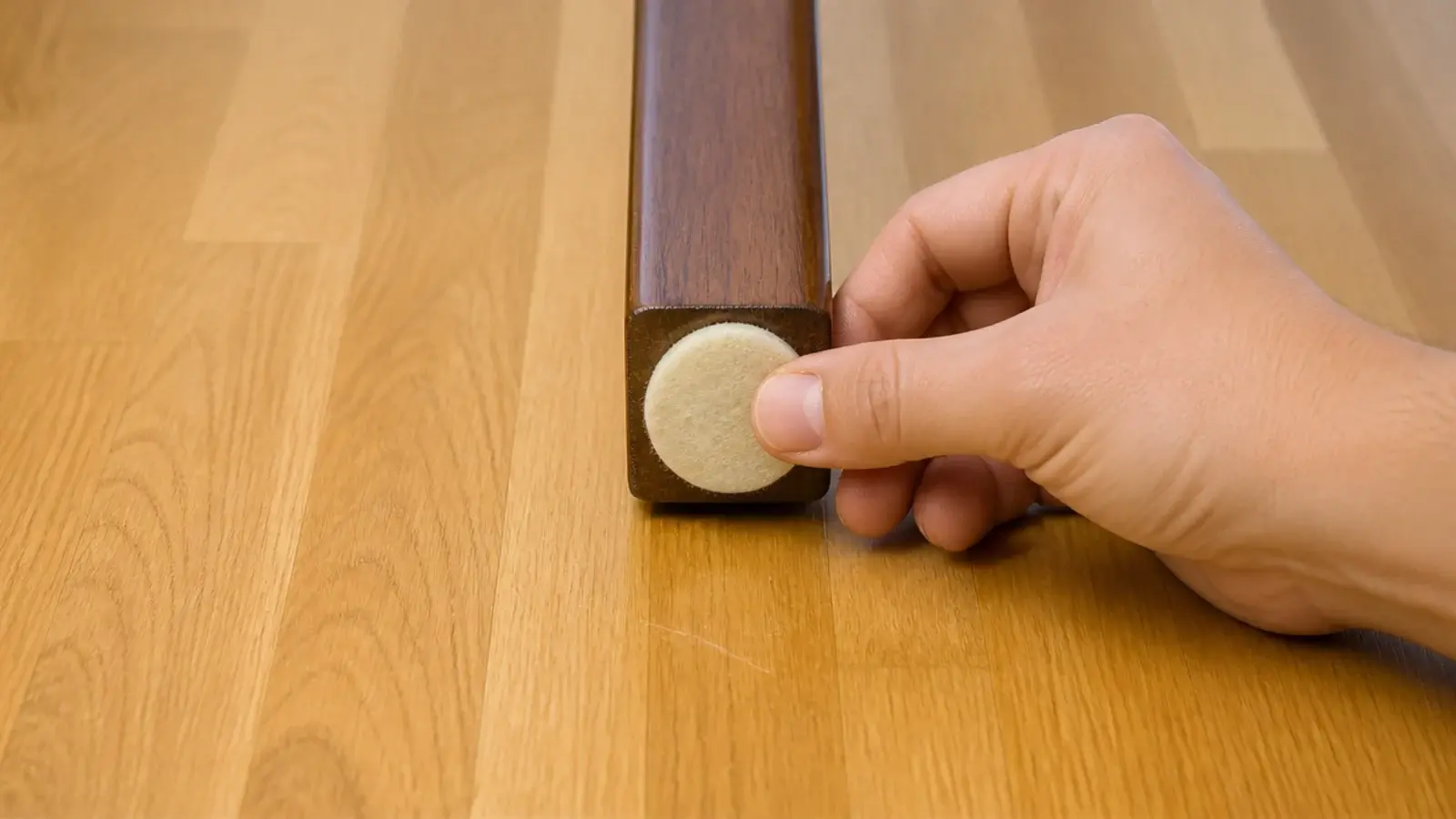 felt pad being pressed onto a table foot above a rented wooden floor